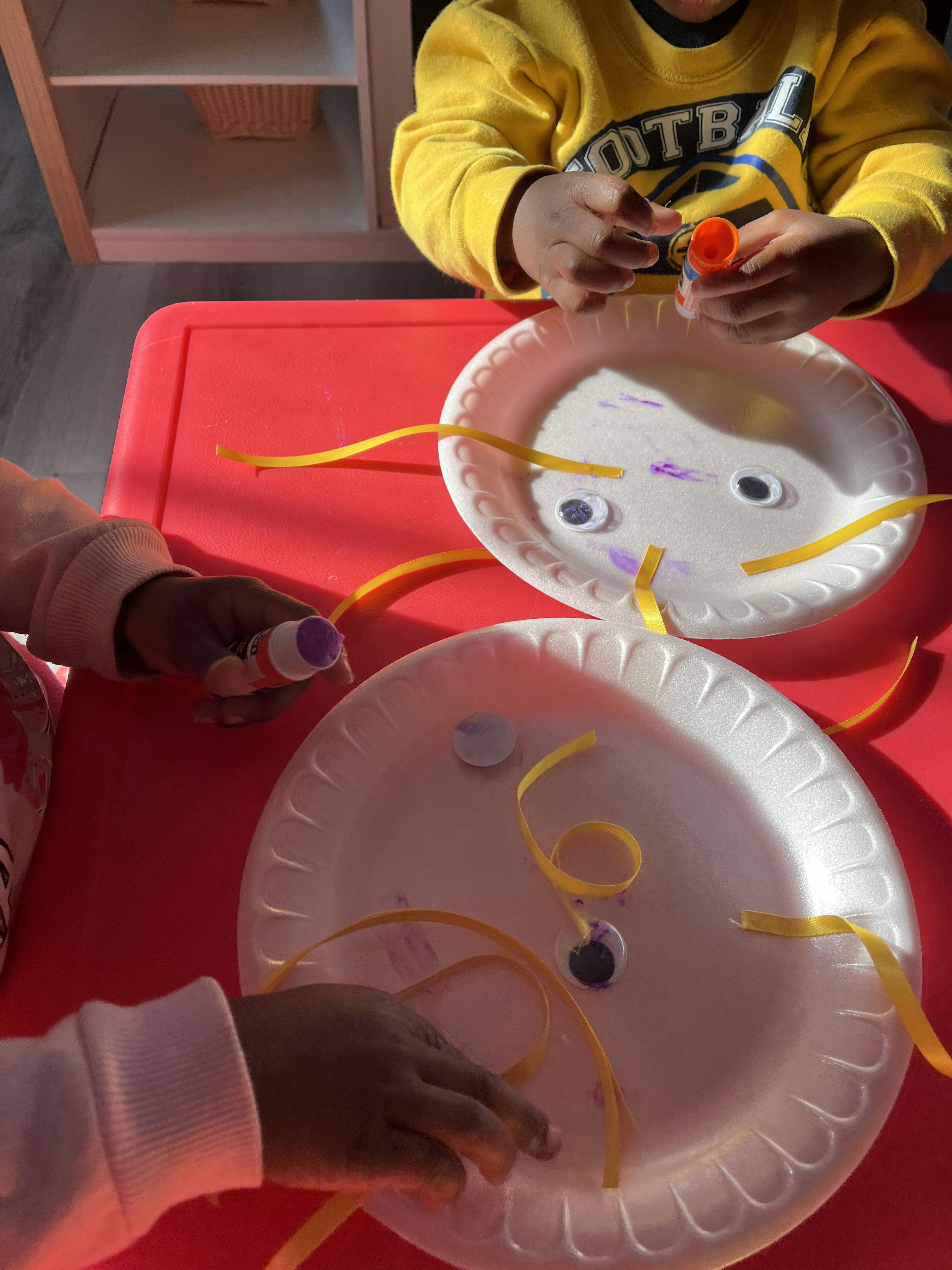 Children crafting with glue and paper plates at a red table