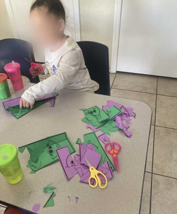 Child using scissors to cut out paper shapes at a table