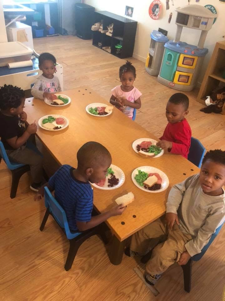 Children sitting at a table with plates of food in a classroom