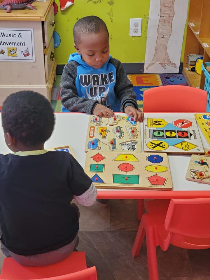 Child playing with shape puzzles at a table in a classroom