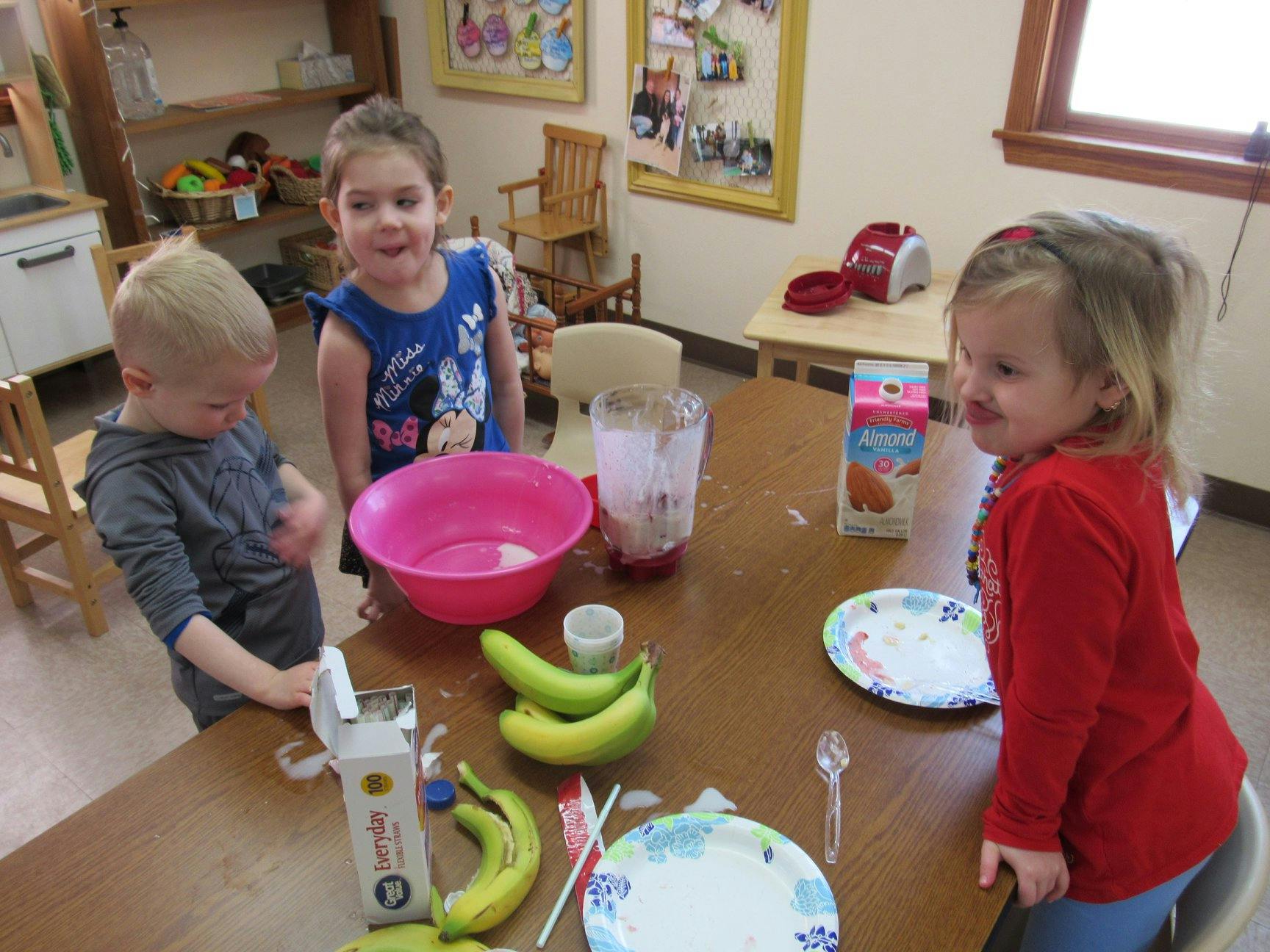 Three children at a table with bananas, a bowl, and a blender