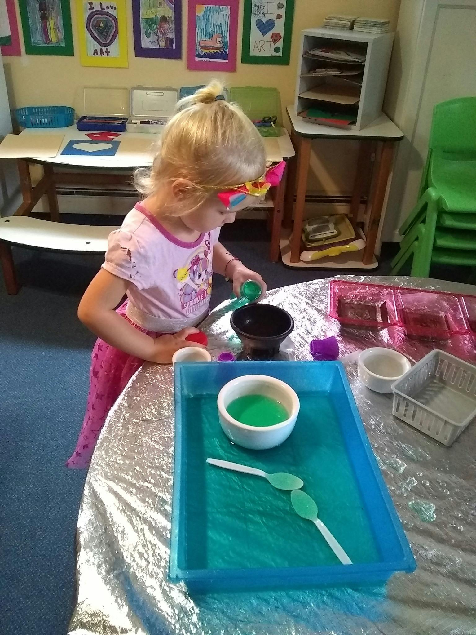 Child playing with green liquid and bowls at a table