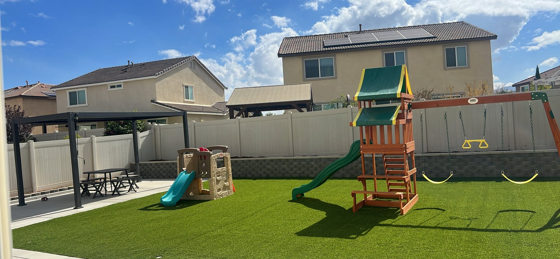 Backyard with artificial grass, a swing set, and a small playhouse