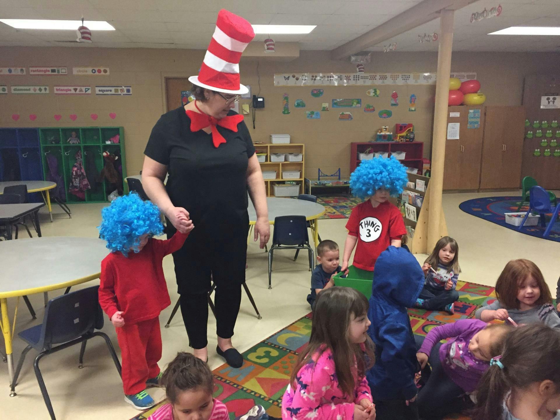 Person in tall striped hat and bow tie holding hands with a child in a blue wig