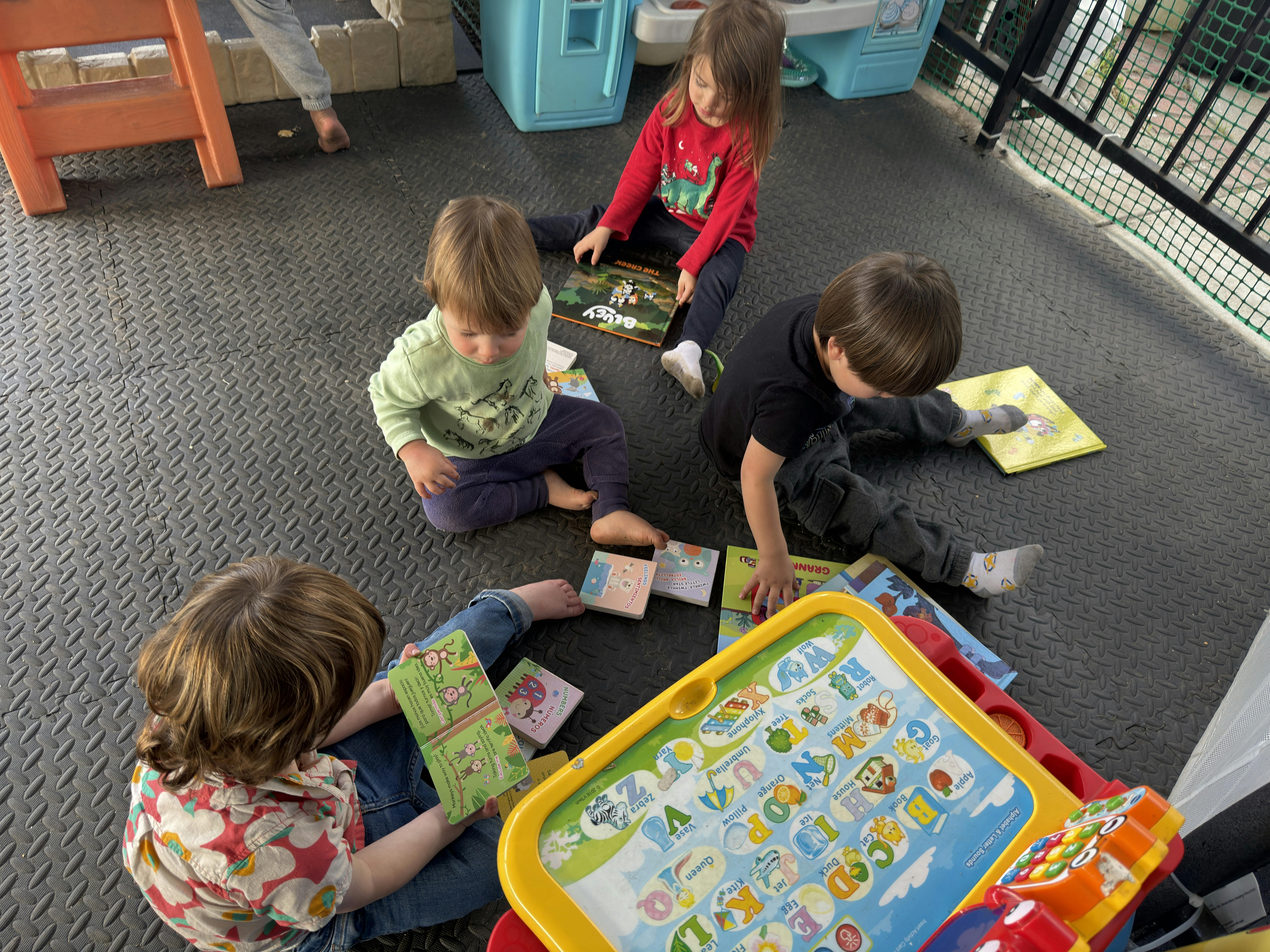 Four children sitting on the floor reading books and playing with an alphabet toy