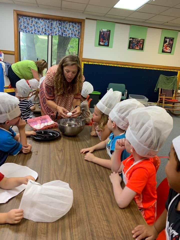 Adult cracking an egg into a bowl with children in chef hats watching