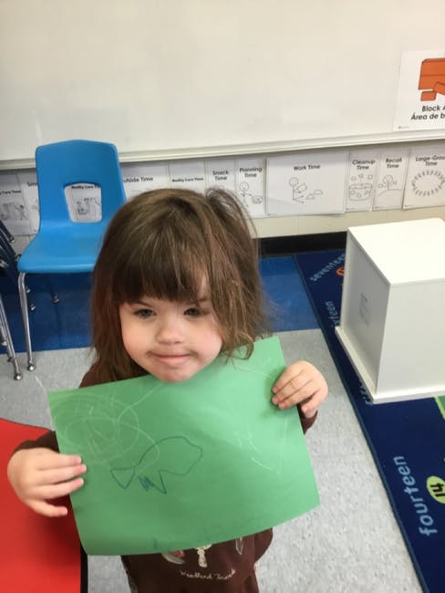 Child holding up a green paper with a drawing on it
