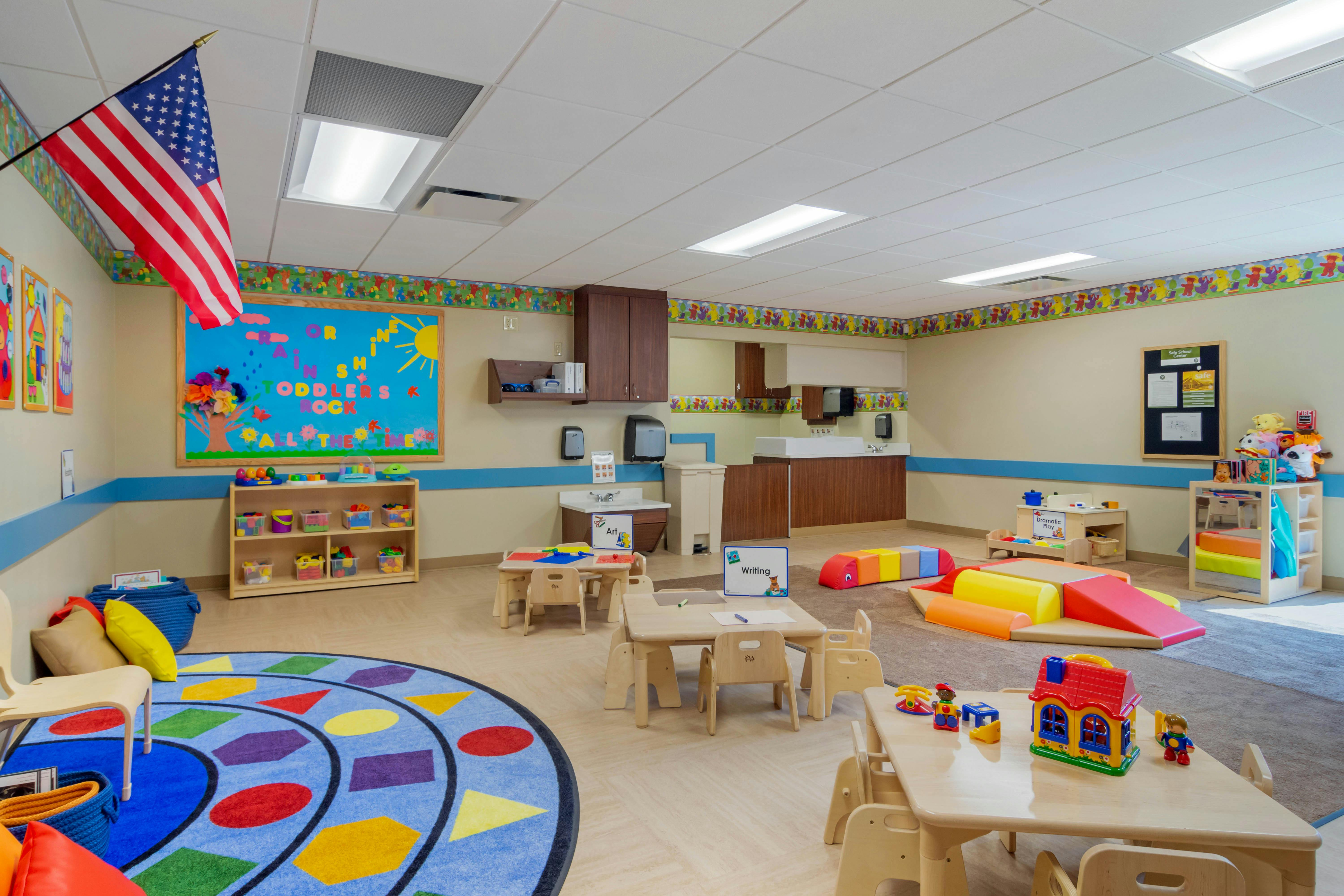 Empty colorful preschool classroom with small tables, chairs, and play areas