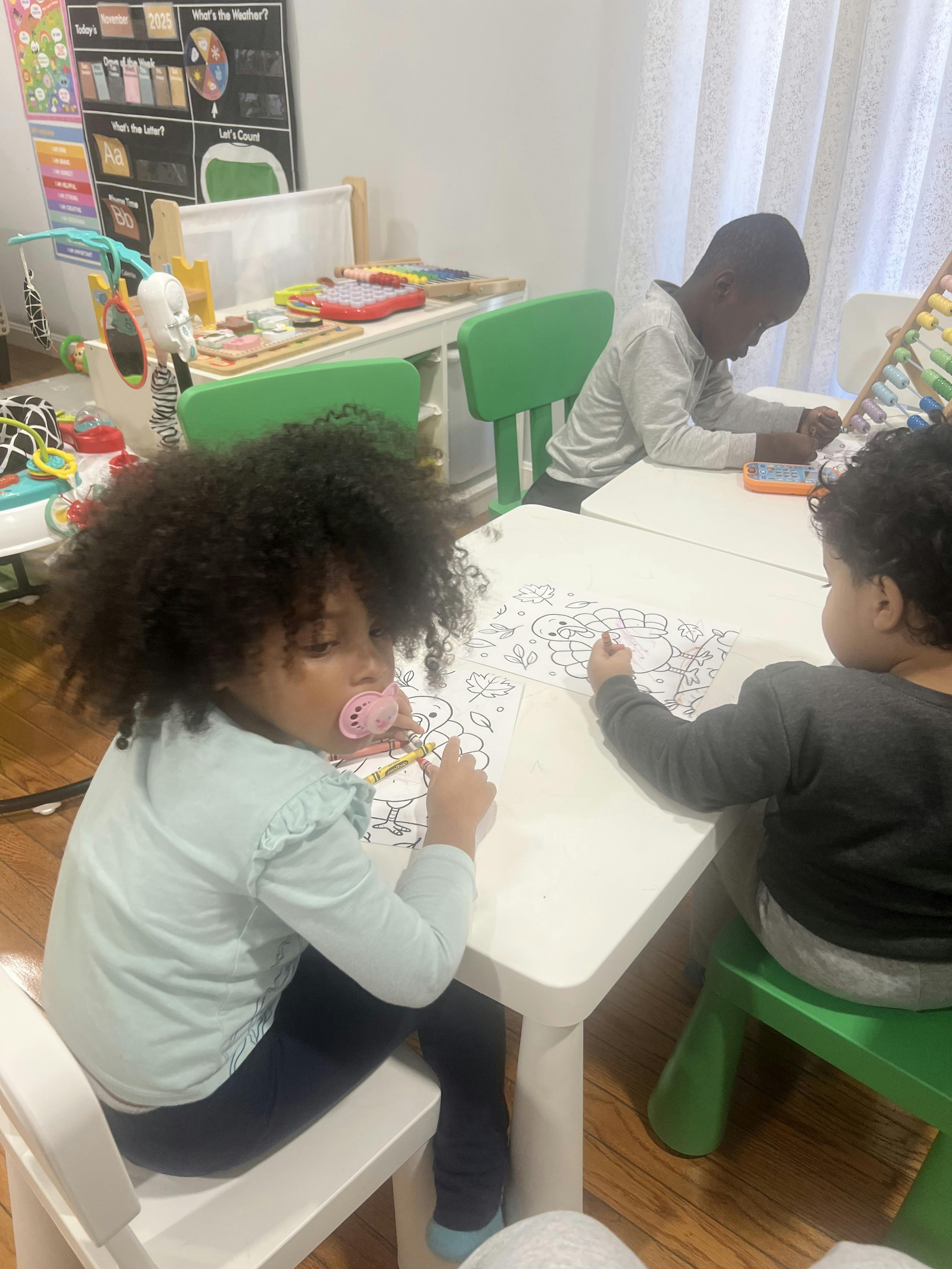 Three children sitting at white tables, coloring and playing with an abacus