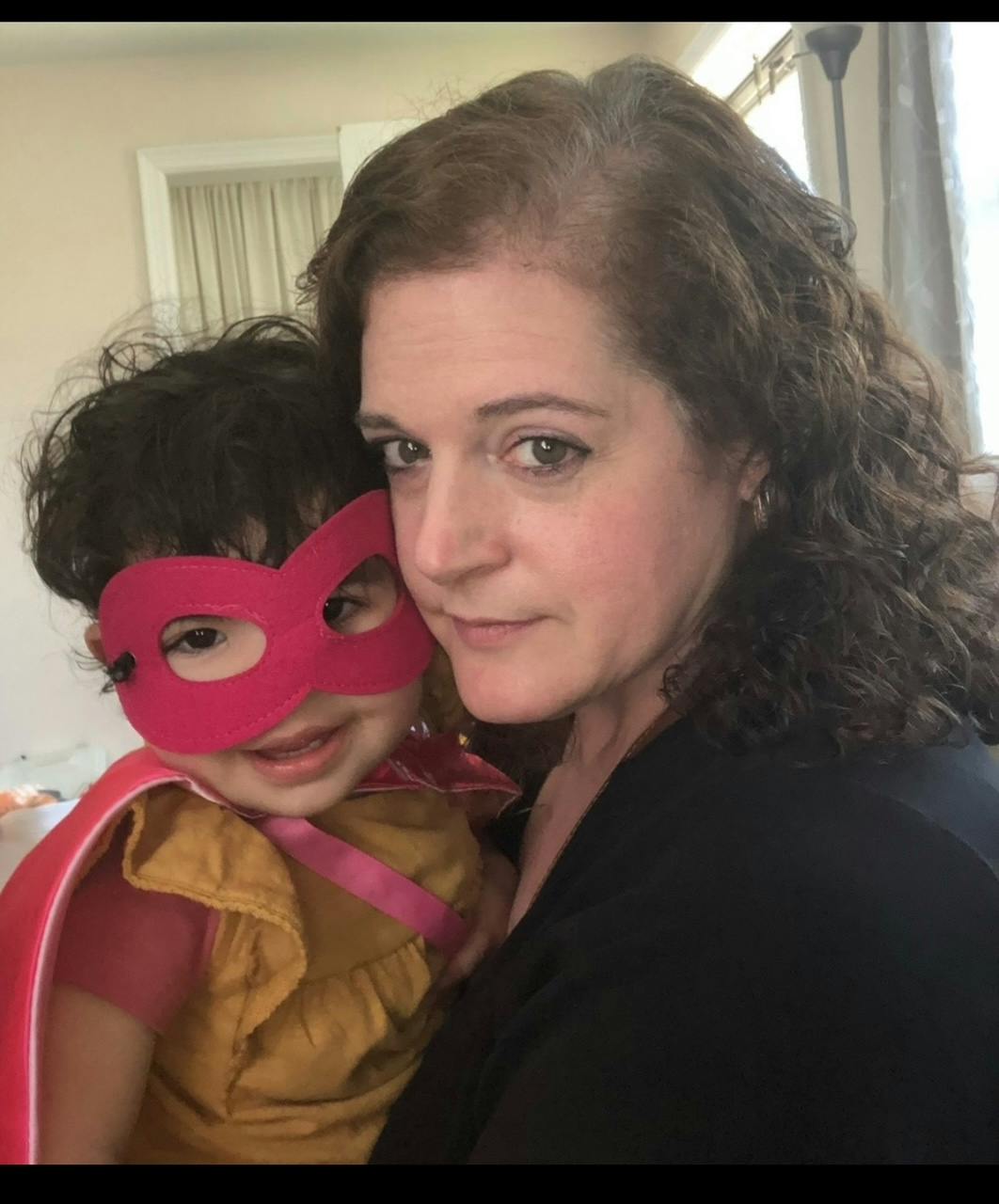 Person holding a child in a superhero mask and cape