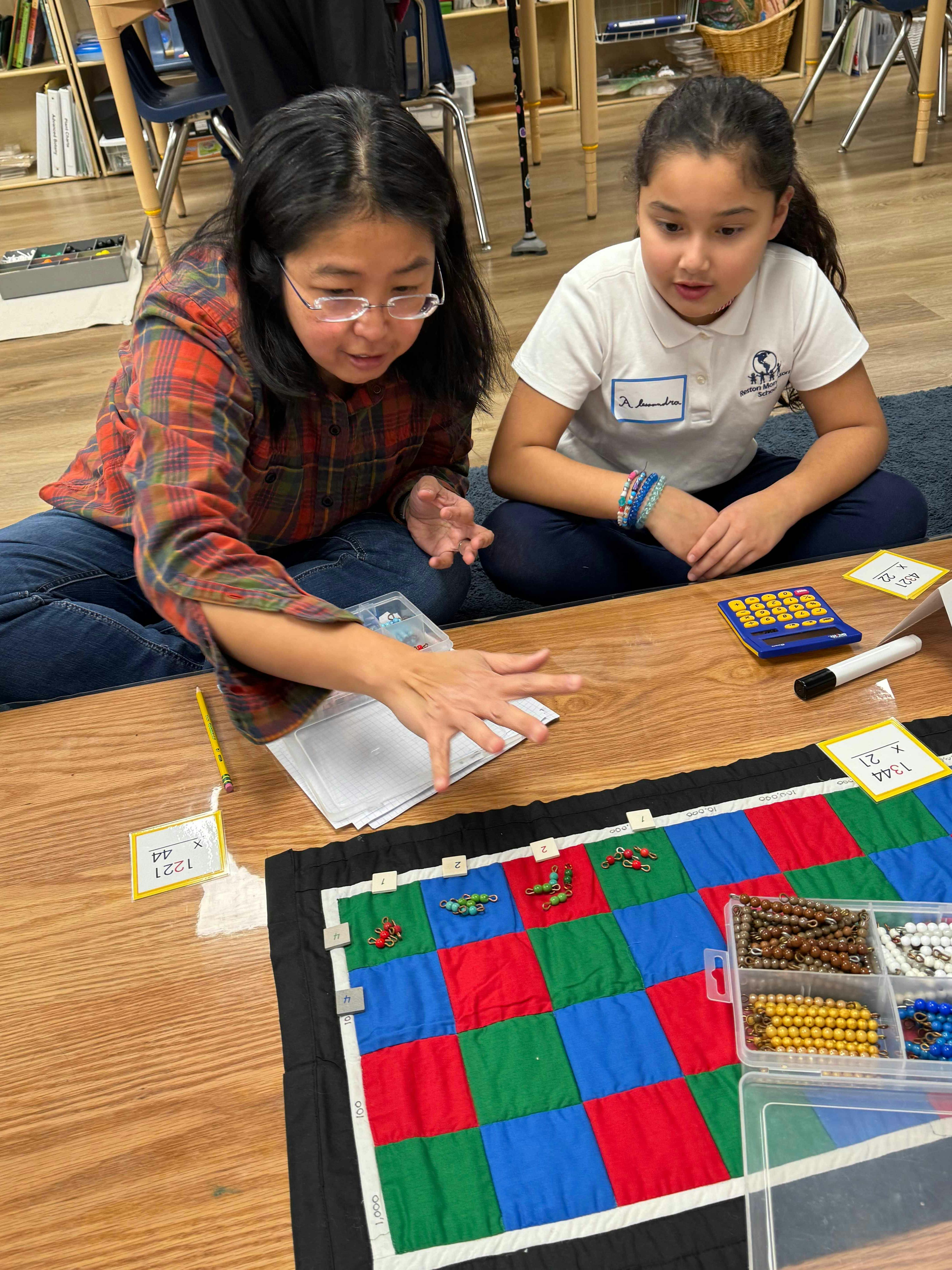Two people sitting on the floor working with a colorful mat and beads