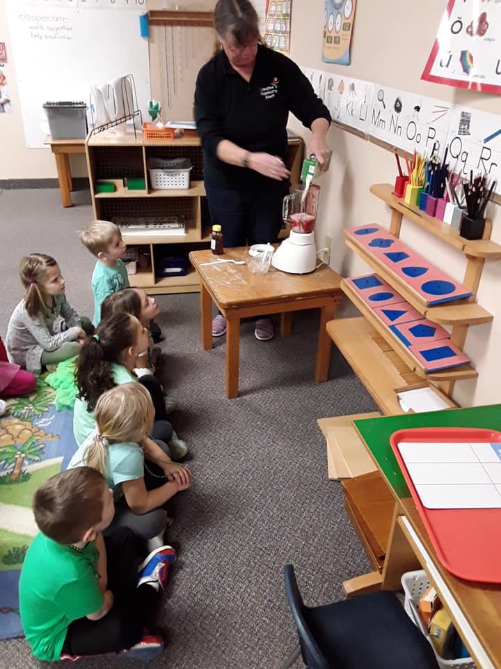 Adult demonstrating a blender to children in a classroom