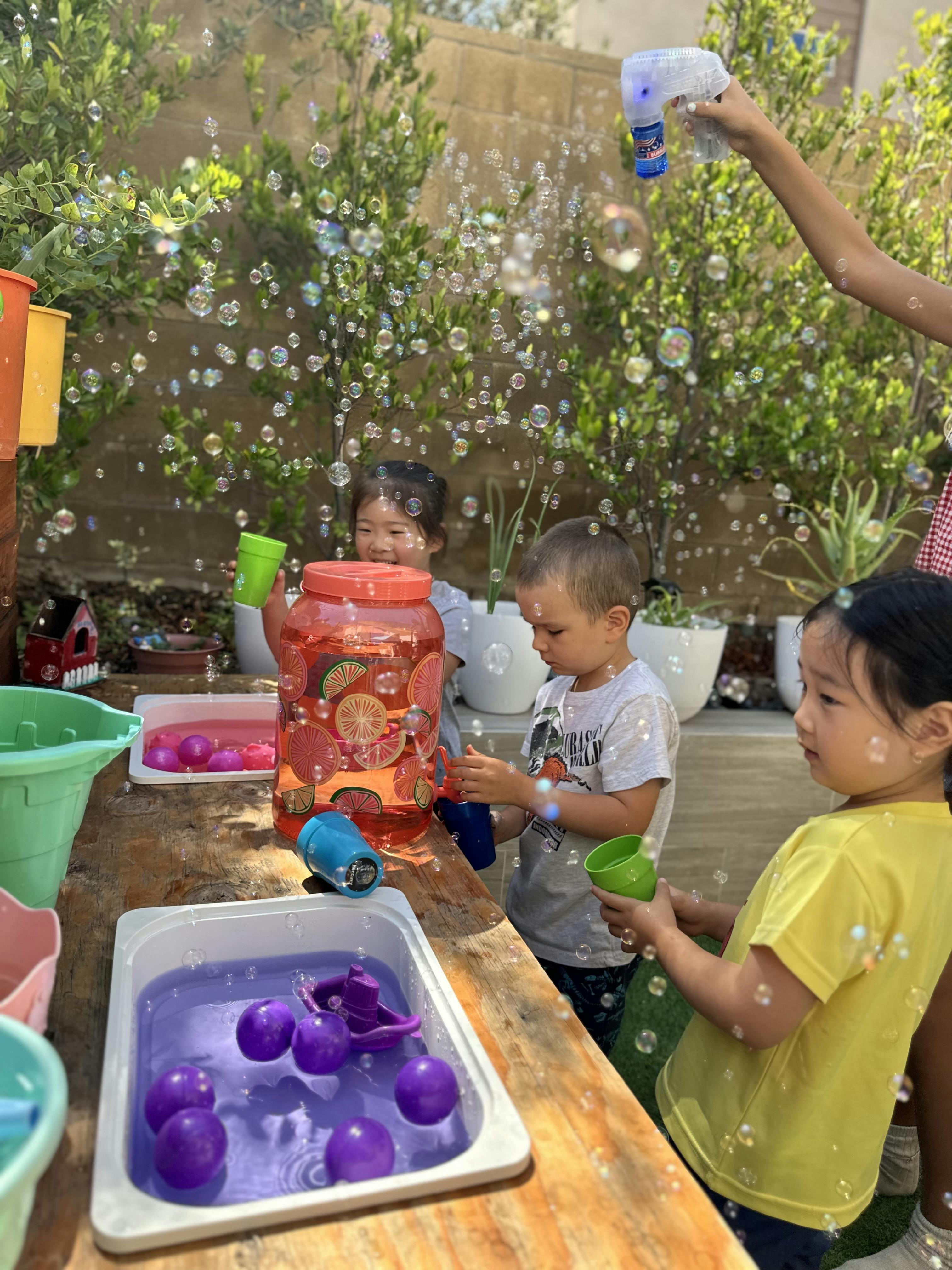 Children playing with soap bubbles and water bins on an outdoor table