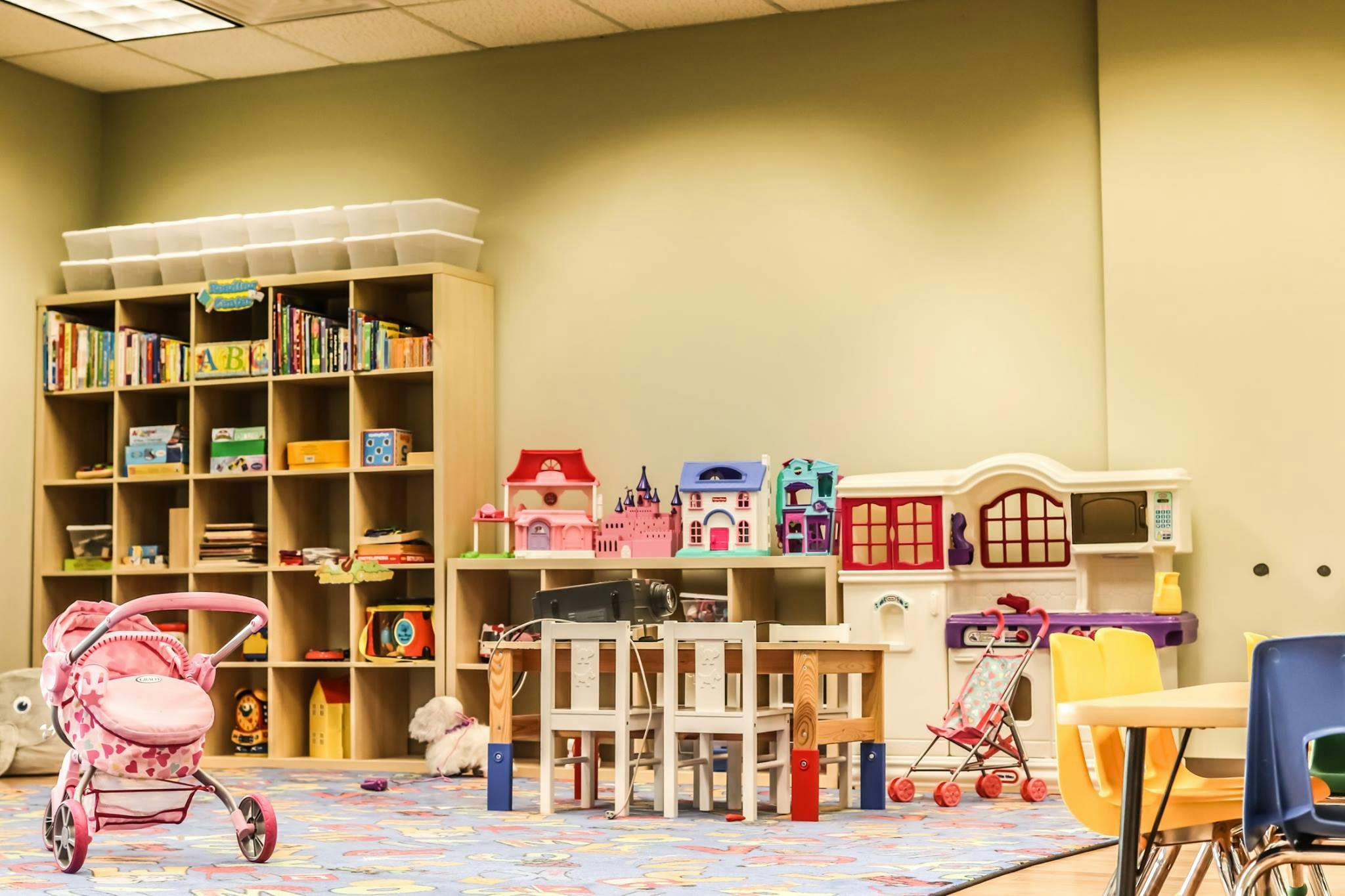 Playroom with toy houses, tables, chairs, and a bookshelf