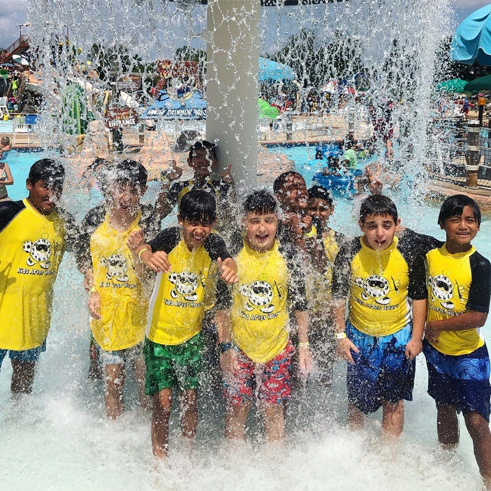 Group of children in yellow shirts standing under a water feature