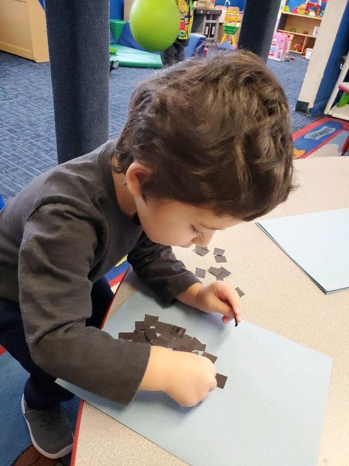 Child placing small dark squares on a light blue paper