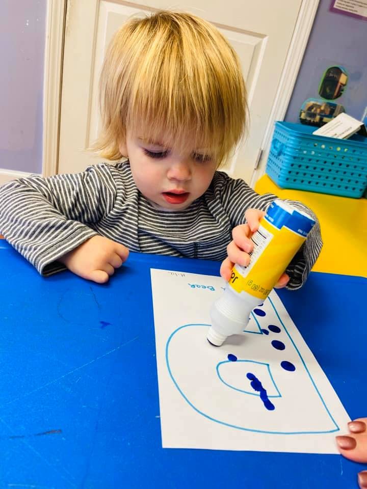 Child using a dot marker on a paper with a letter outline