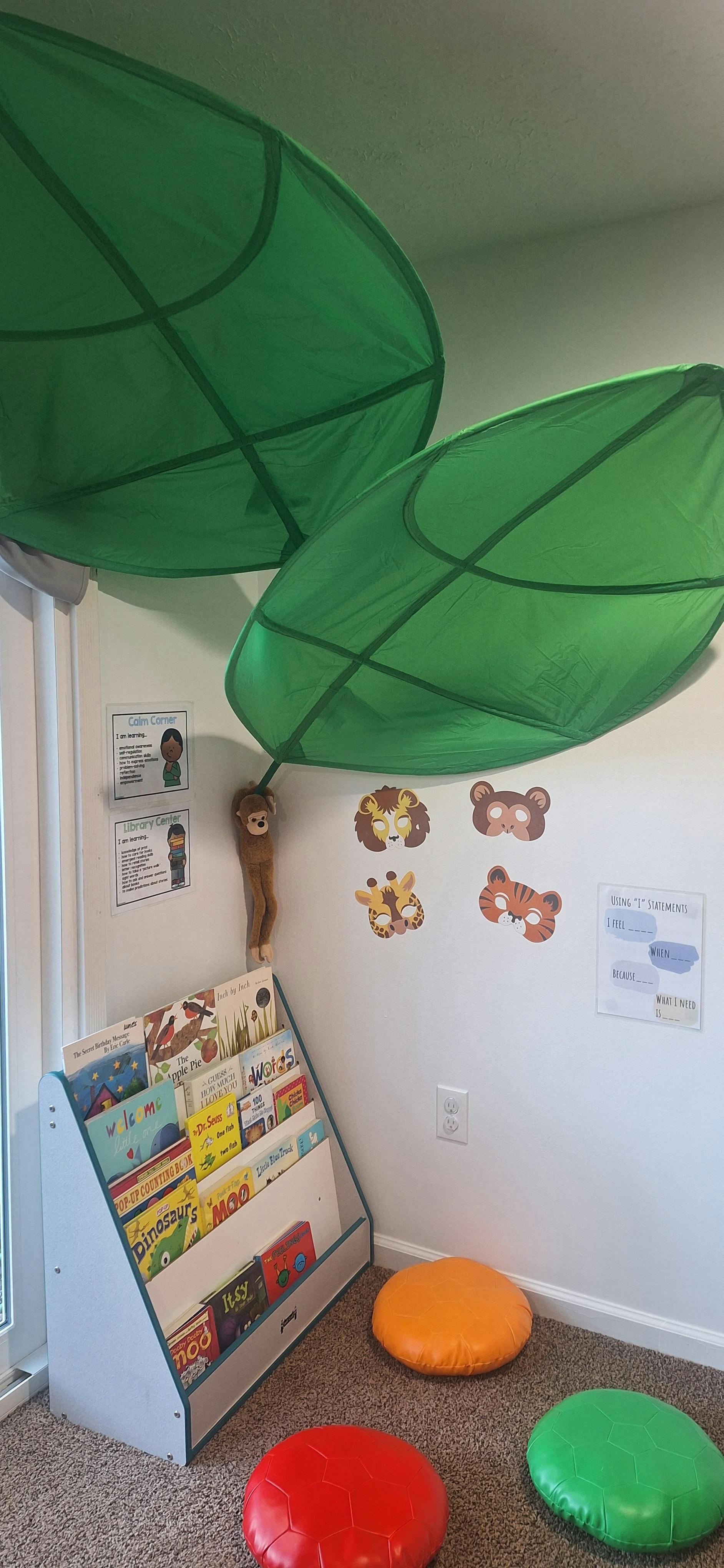 Children's room with green leaf decorations, wall decals, book display, and floor cushions
