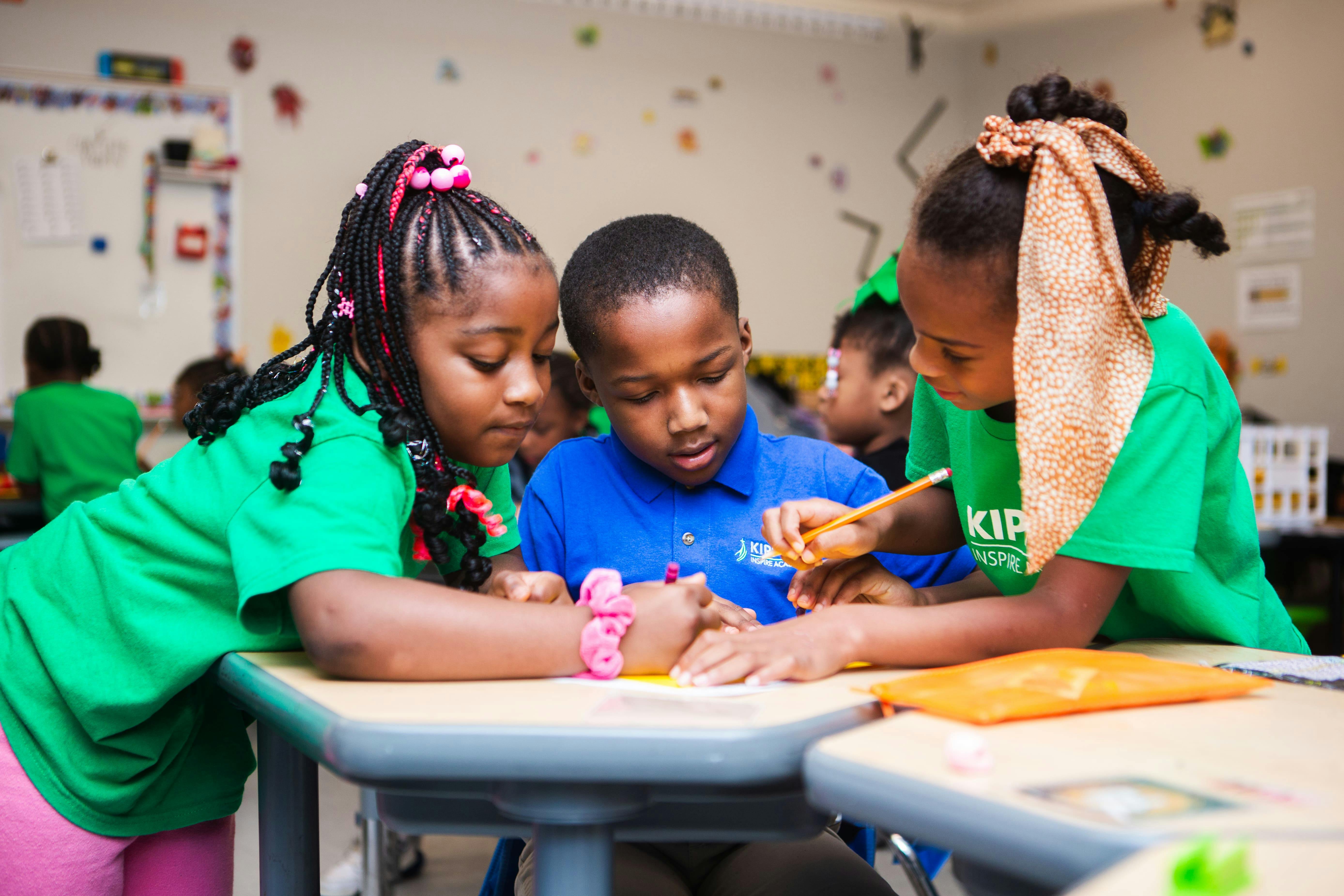 Three children working together at a desk in a classroom