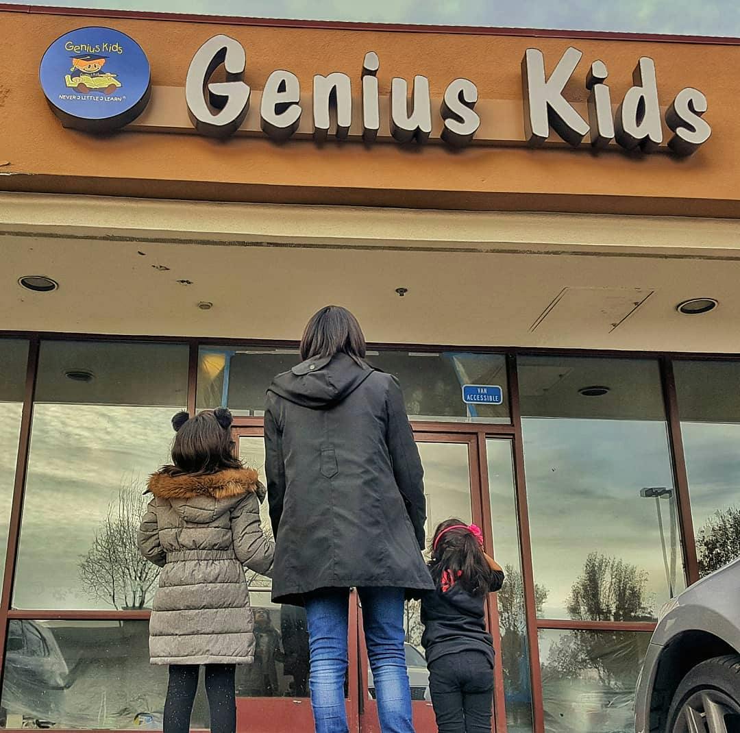 Person and two children looking at a building with "Genius Kids" sign