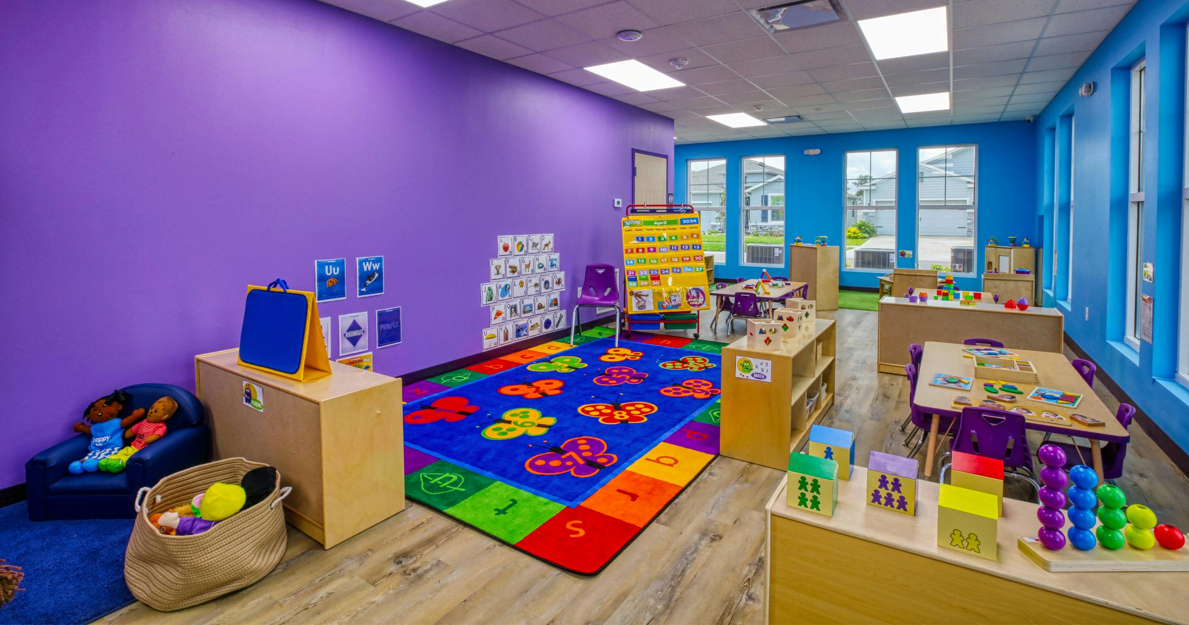 Classroom with purple walls, a butterfly rug, small tables and chairs, and educational toys