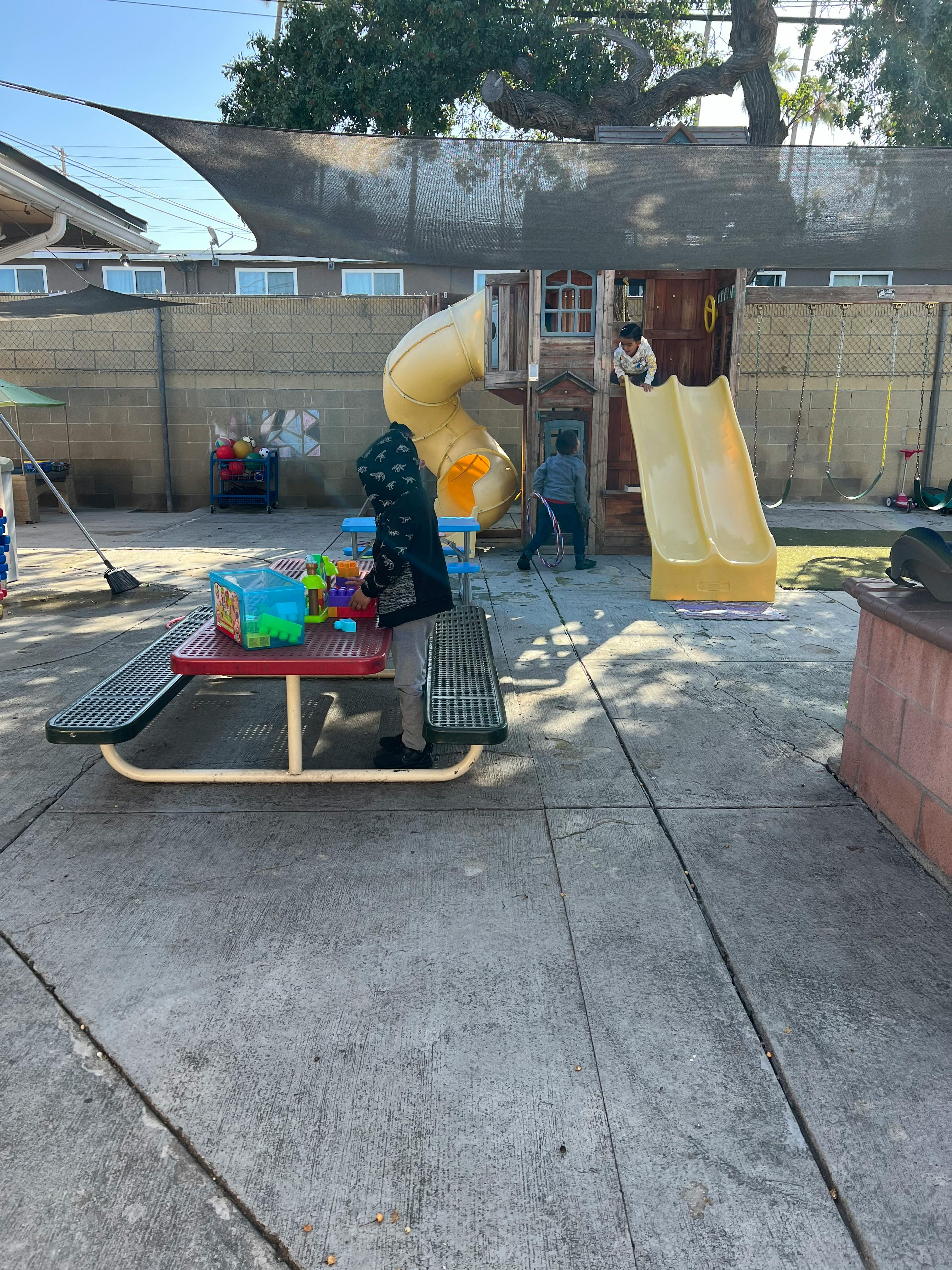 Child standing at a picnic table with toys in a playground