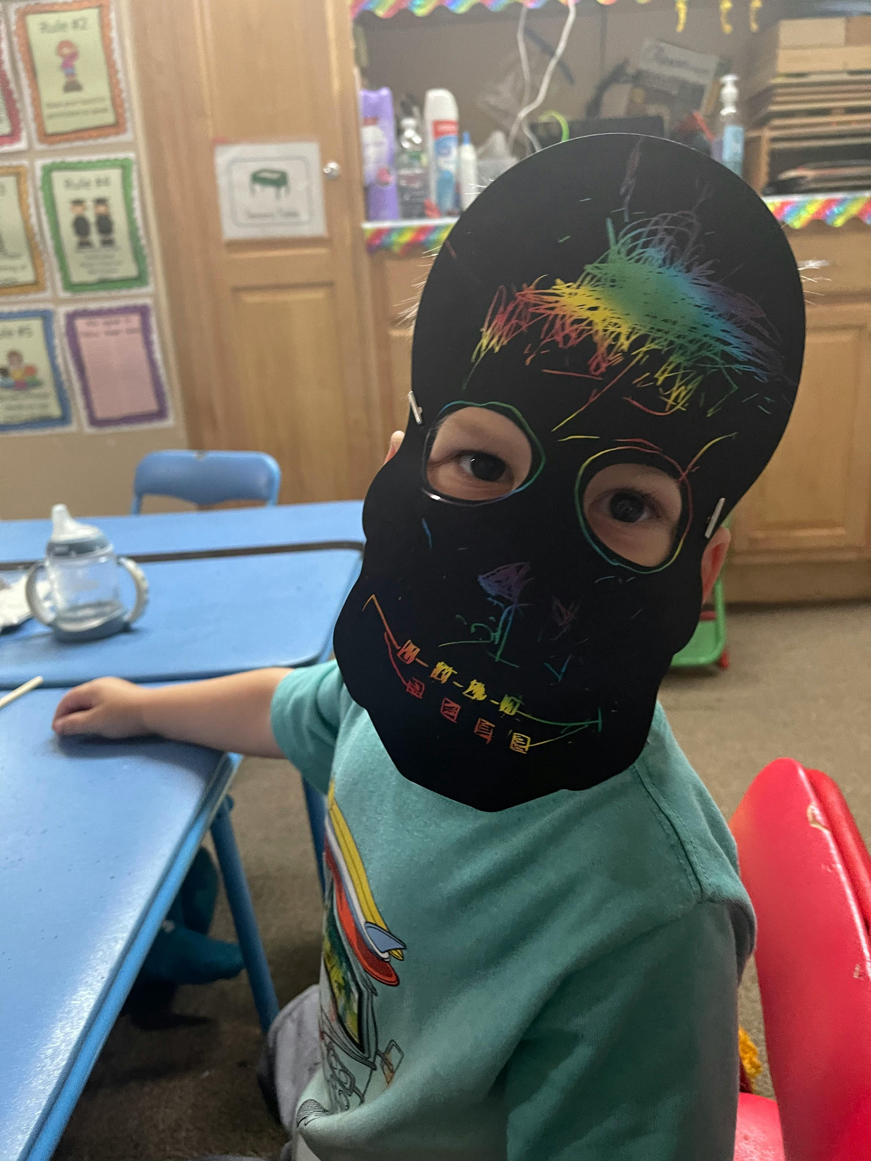 Child wearing a black skull mask with rainbow colors