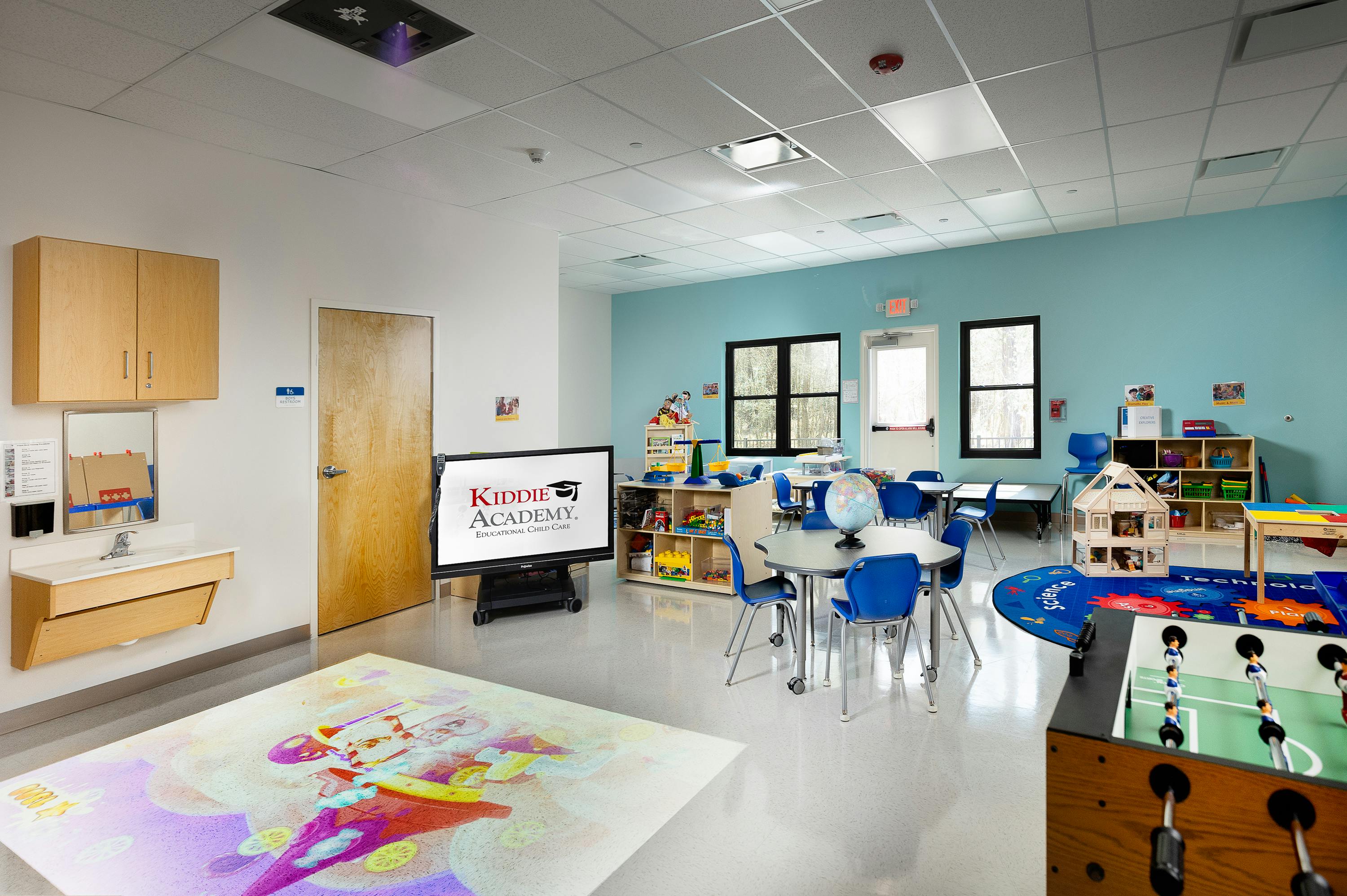 Classroom with small tables and chairs, a TV, and a foosball table