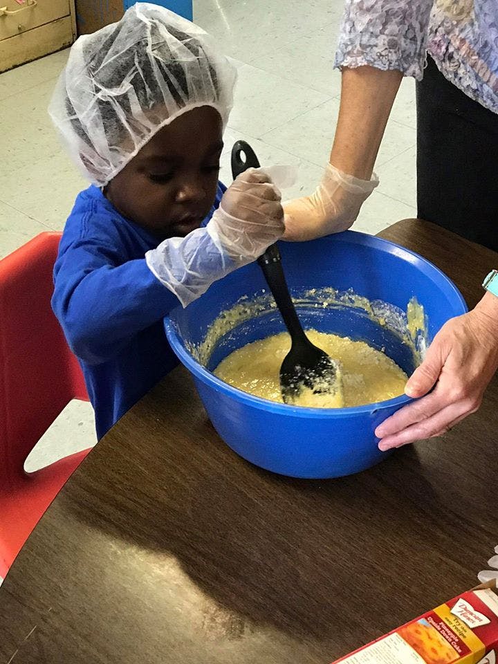 Child and person mixing batter in a blue bowl