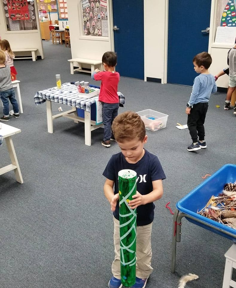 Child holding a green decorated tube in a classroom