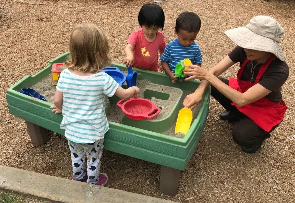 Adult and three children playing in a sandbox