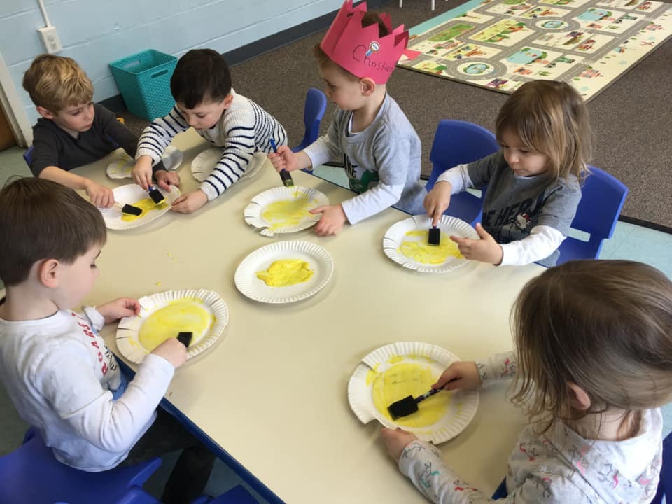 Children painting with yellow paint on paper plates in a classroom