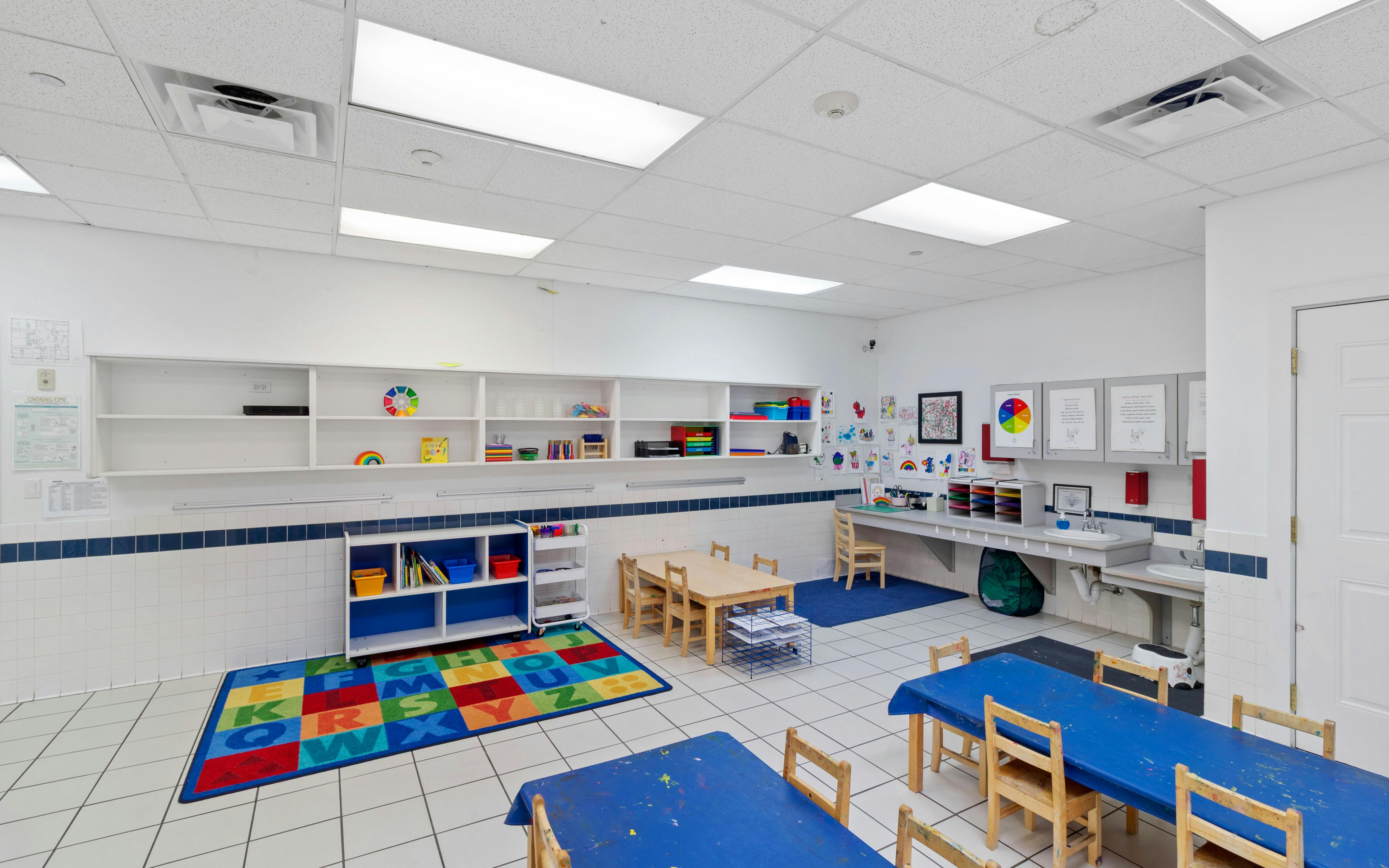 Classroom with small tables and chairs, shelves, and a colorful alphabet rug