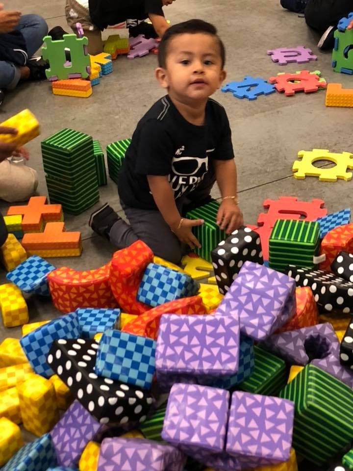 Child kneeling on floor surrounded by colorful soft play blocks