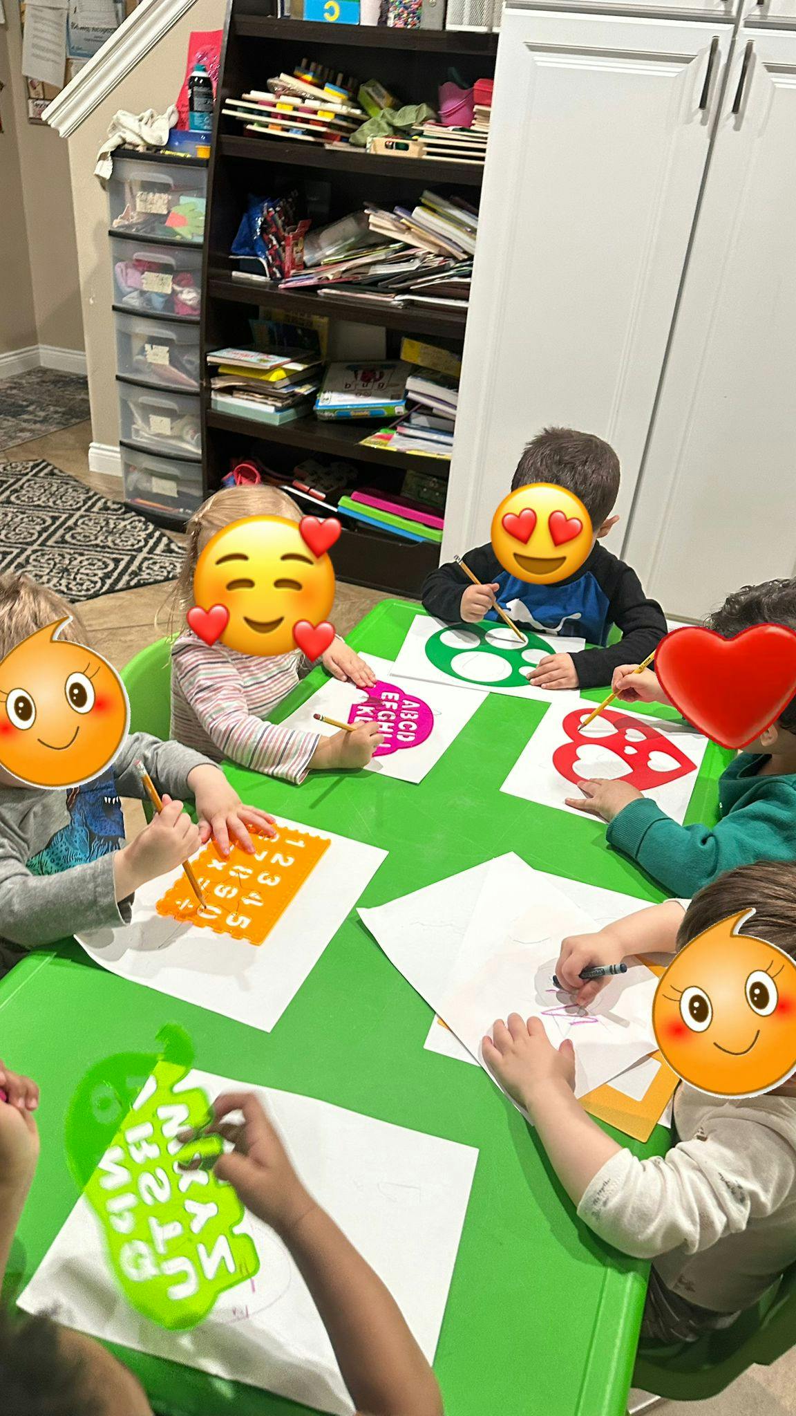 Children drawing and tracing letters at a green table