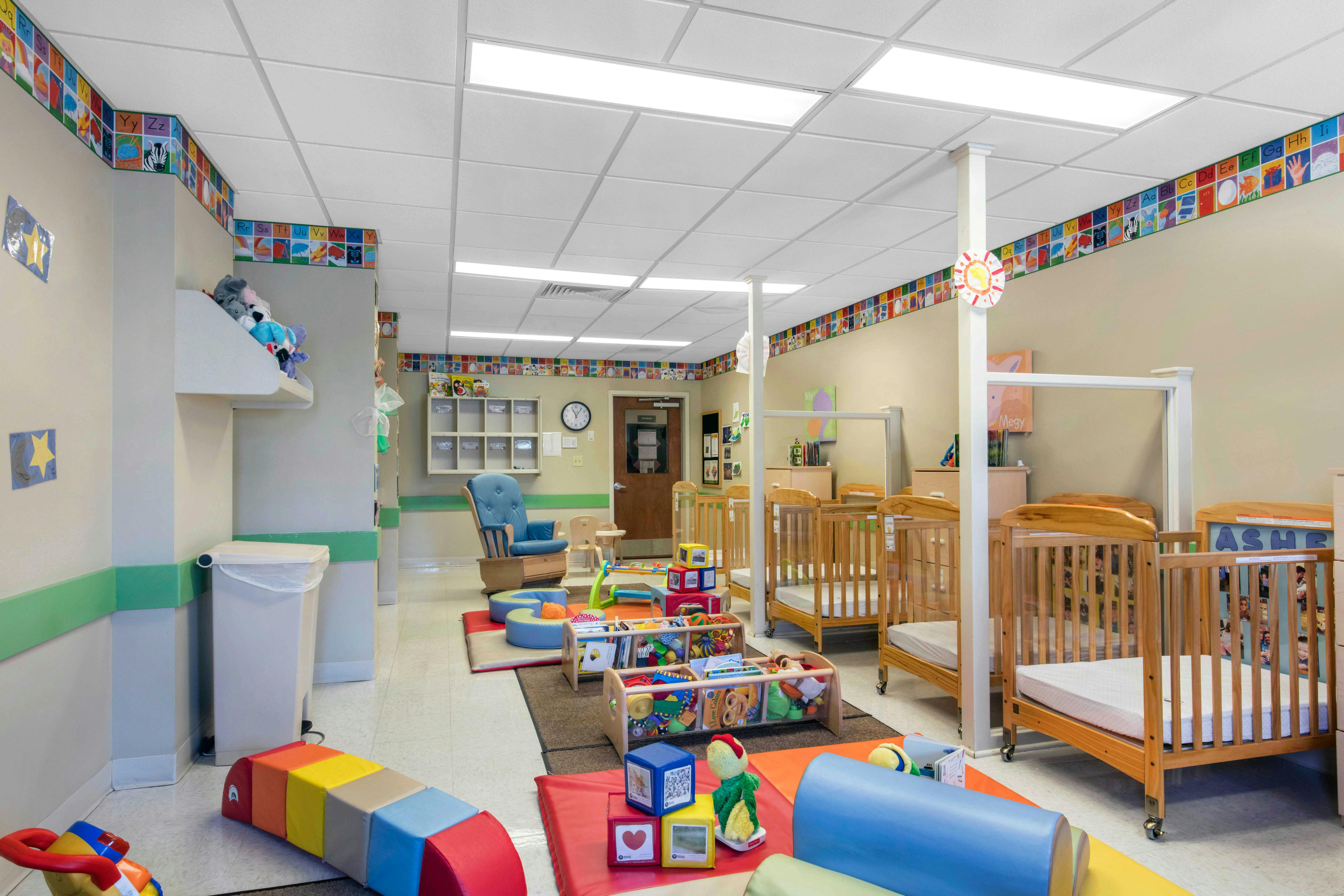 nursery room with multiple cribs, a blue rocking chair, and play mats with blocks