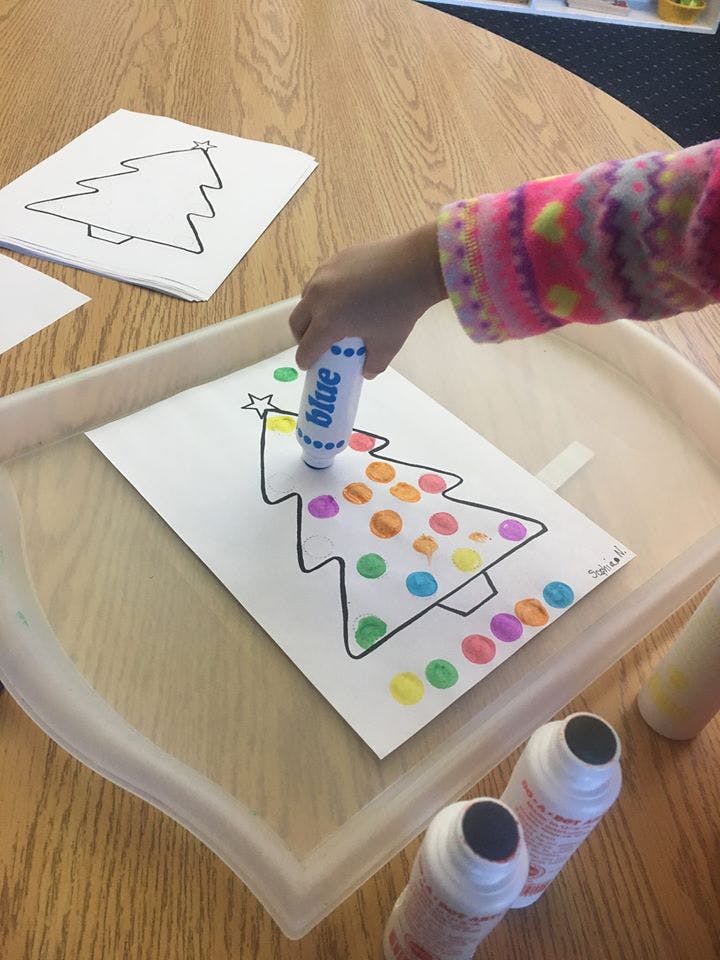 Child decorating a Christmas tree outline with colorful dots