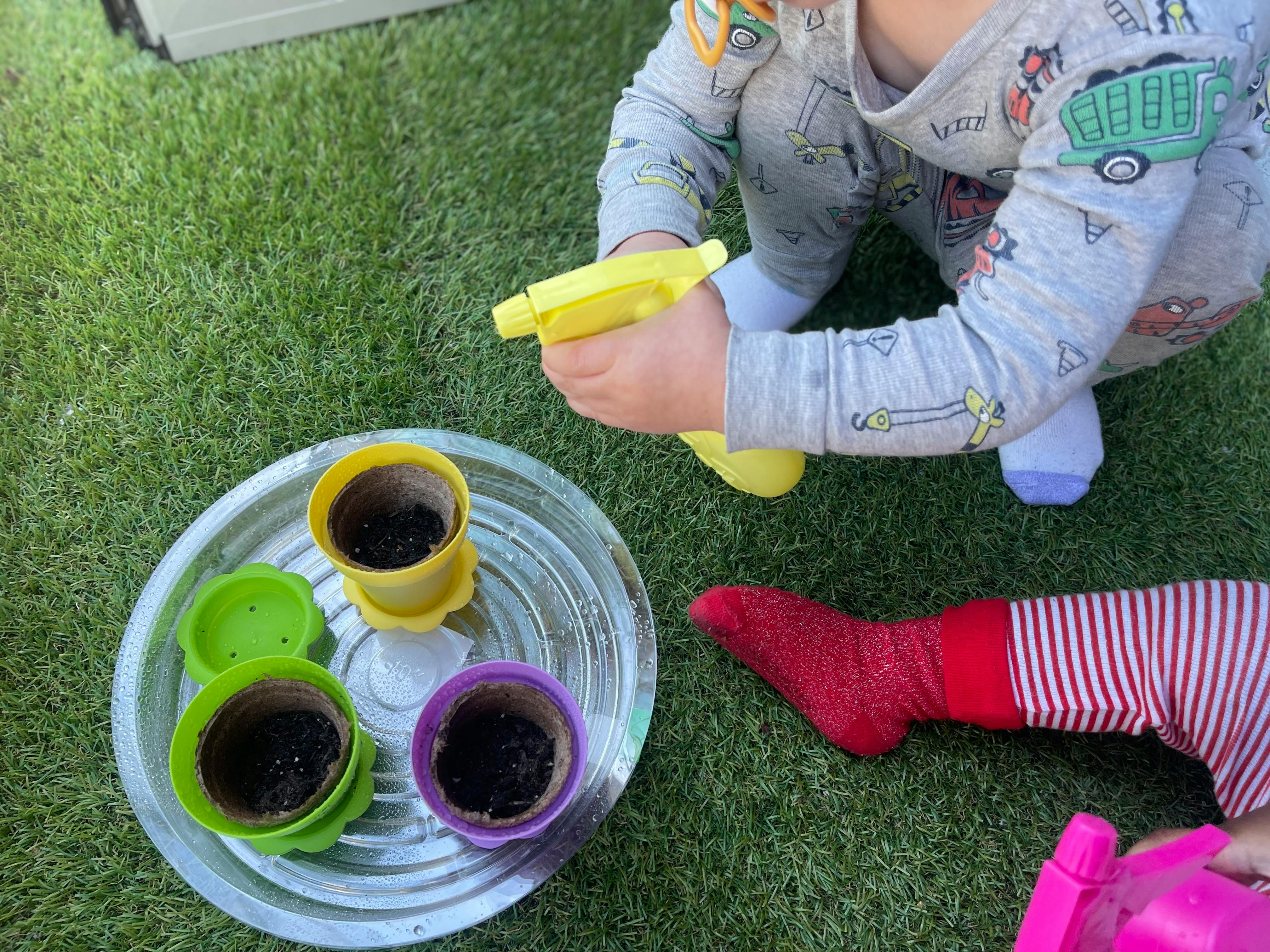 Child in pajamas watering small potted plants with a yellow spray bottle