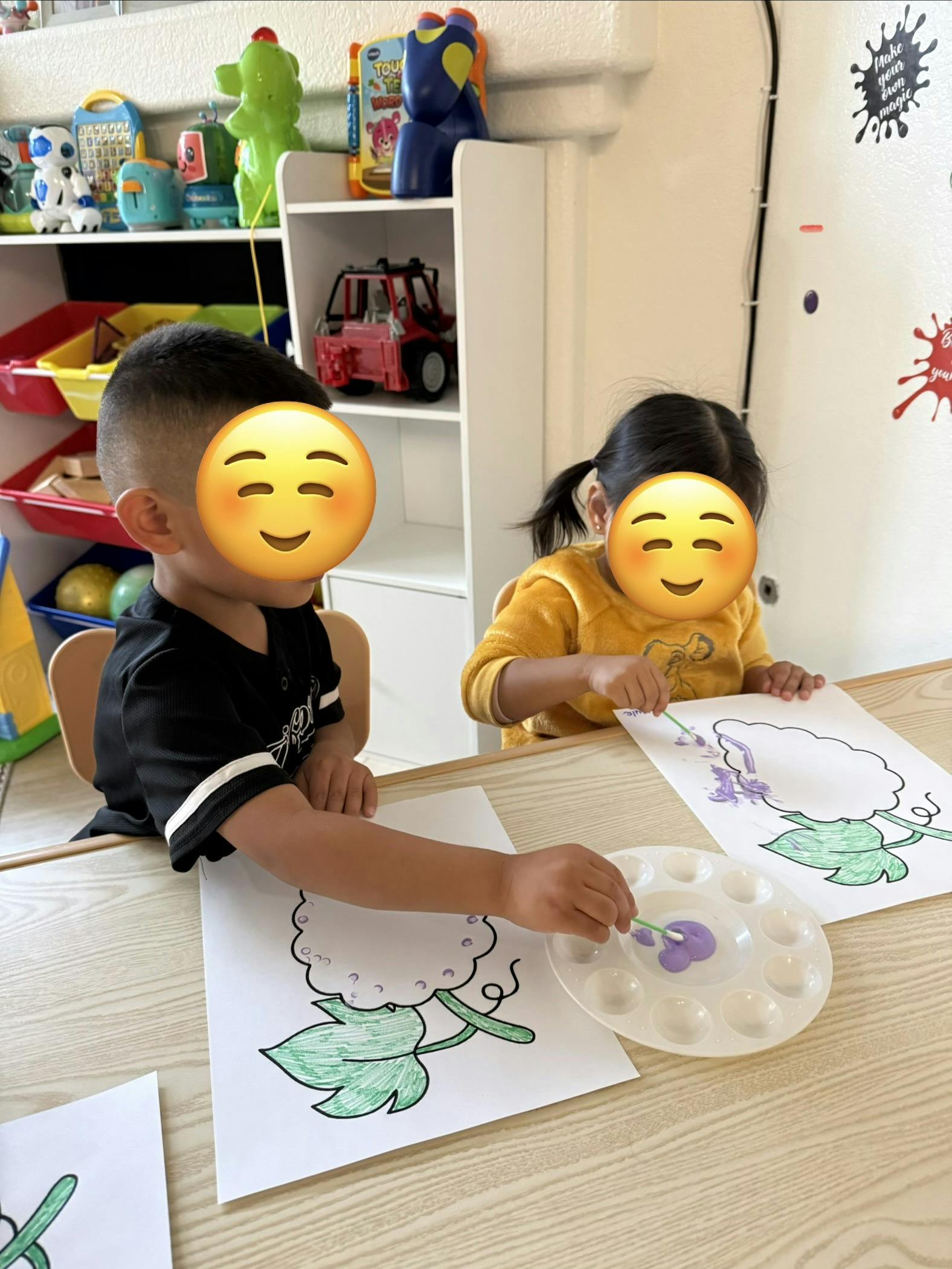 Two children painting plant illustrations at a table in a classroom