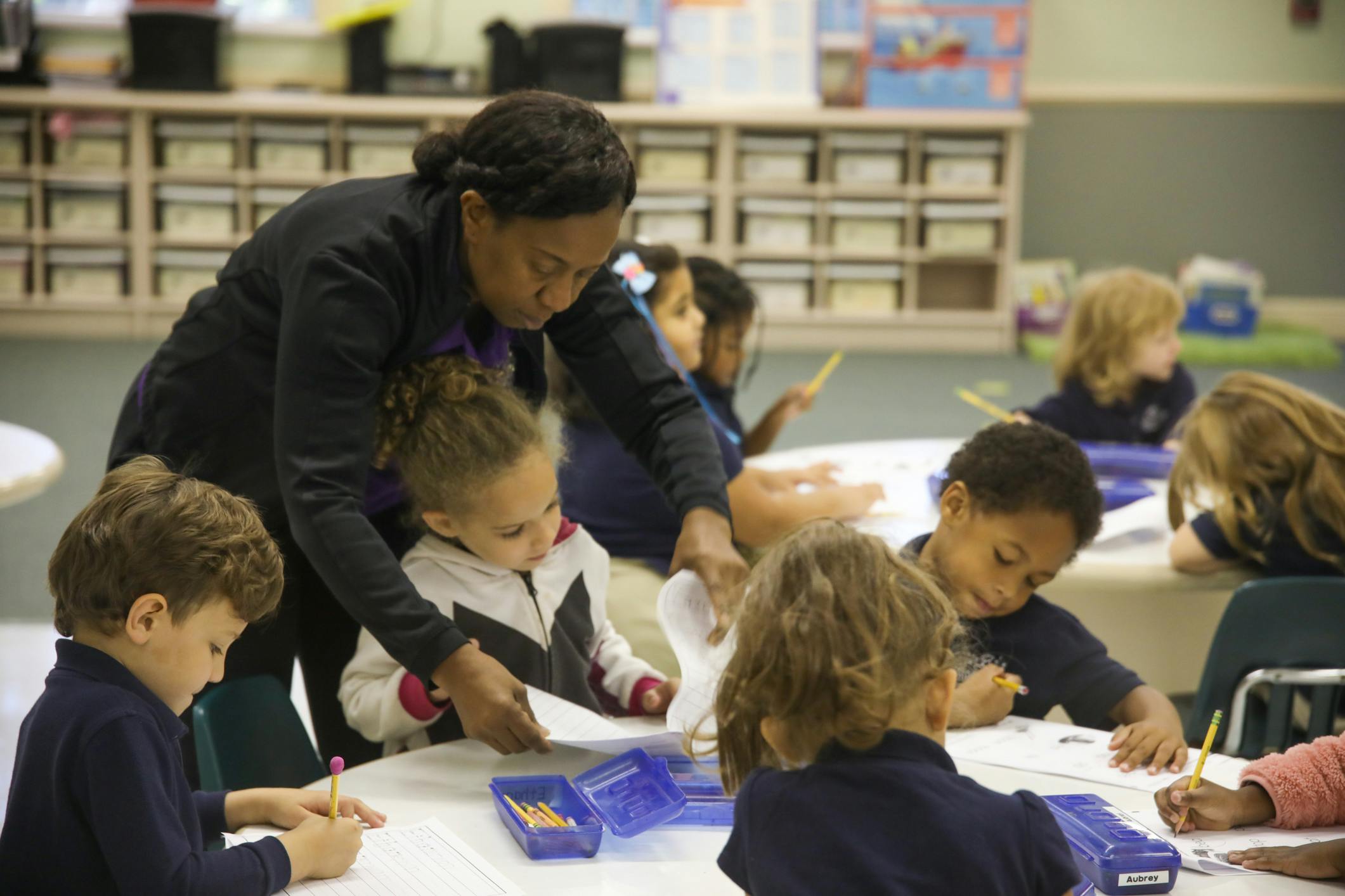 Person helping a child with papers at a table with other children