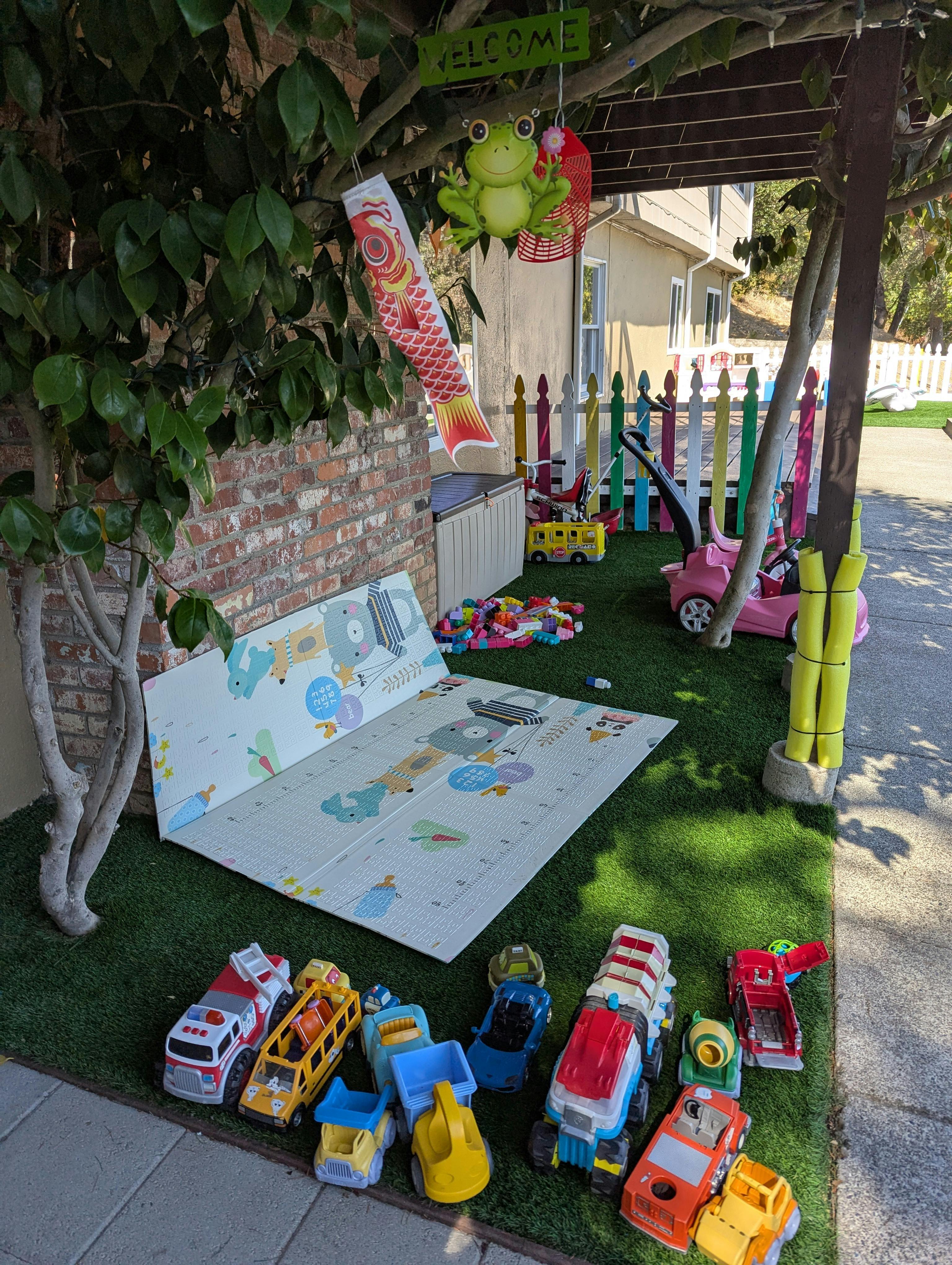 Outdoor play area with toys, a playmat, and colorful fence
