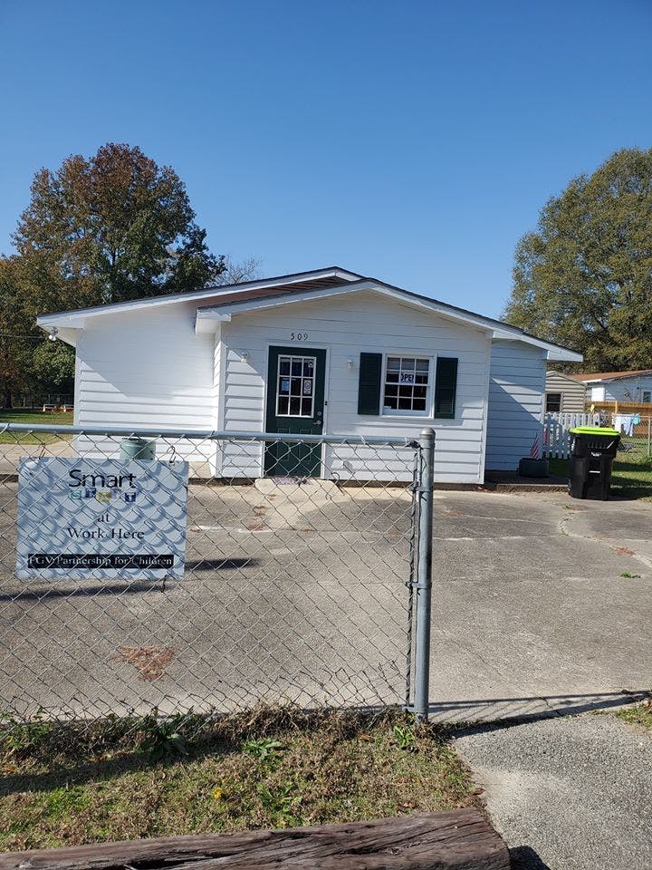 White house with green door and shutters behind a chain link fence