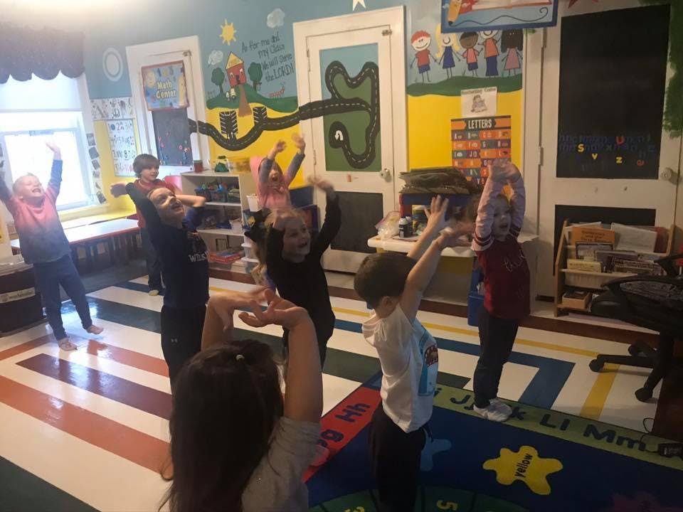 Children in a classroom raising their arms