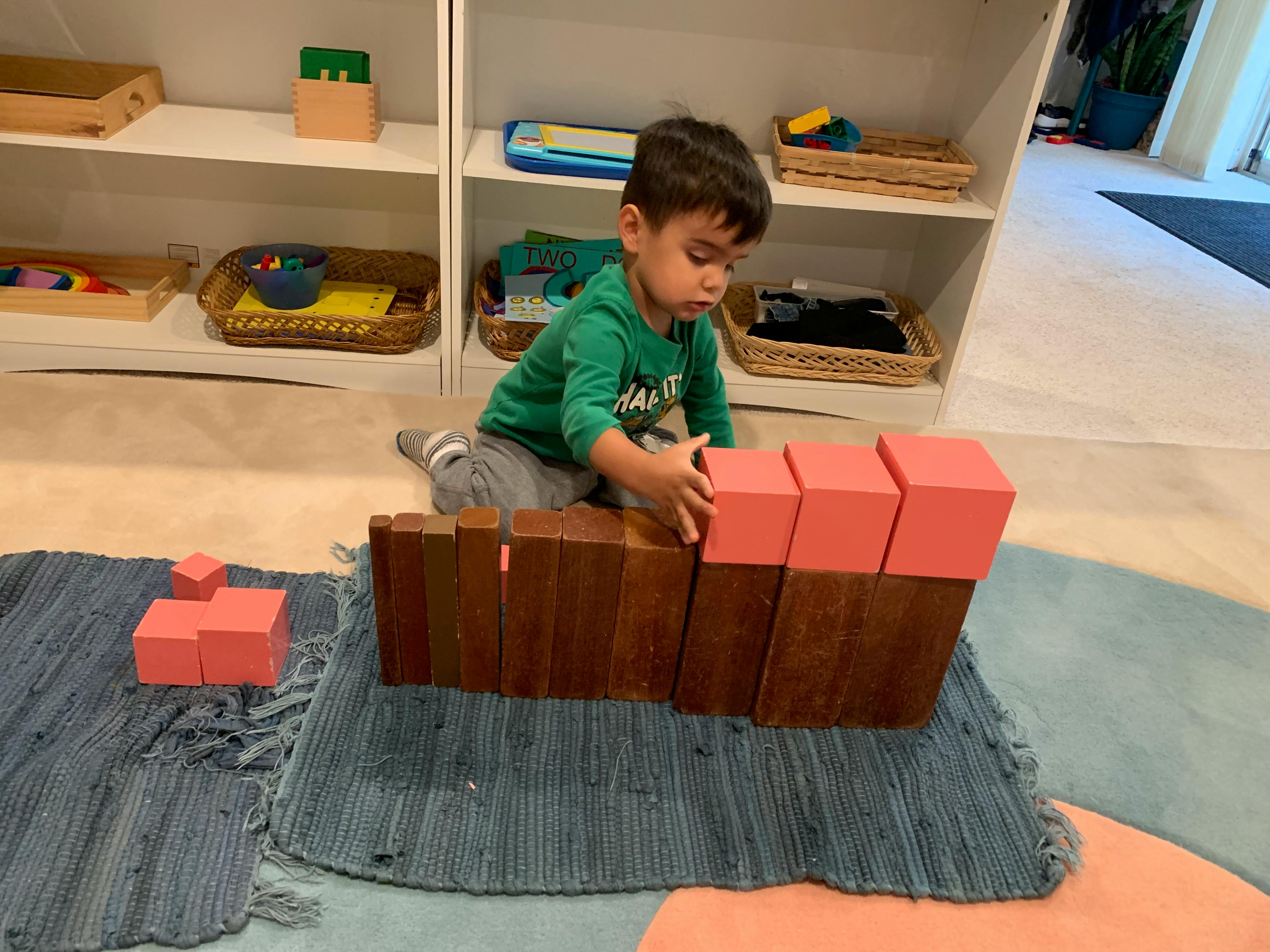 Child playing with wooden and pink blocks on a rug
