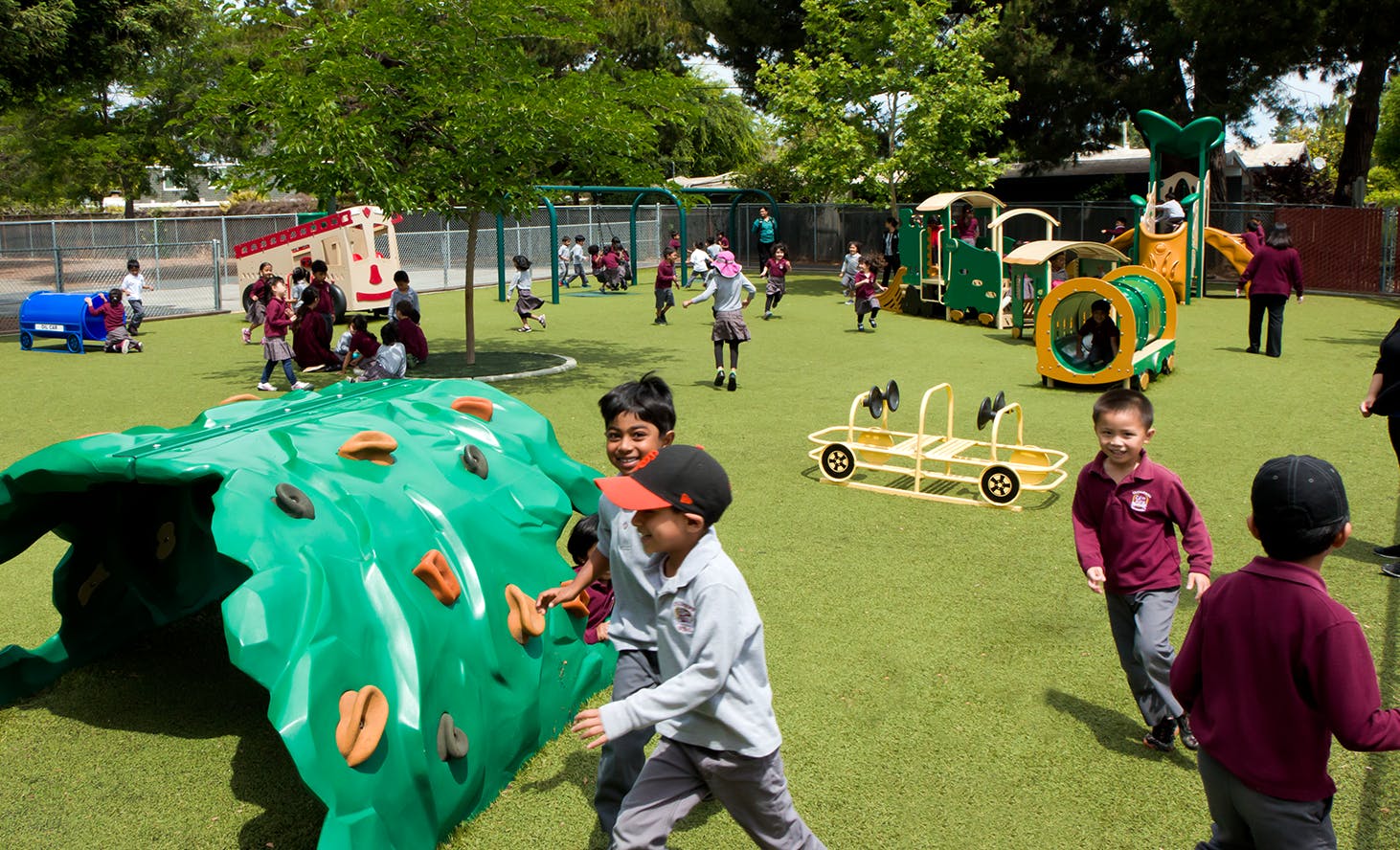 Children playing on a green playground with various play structures