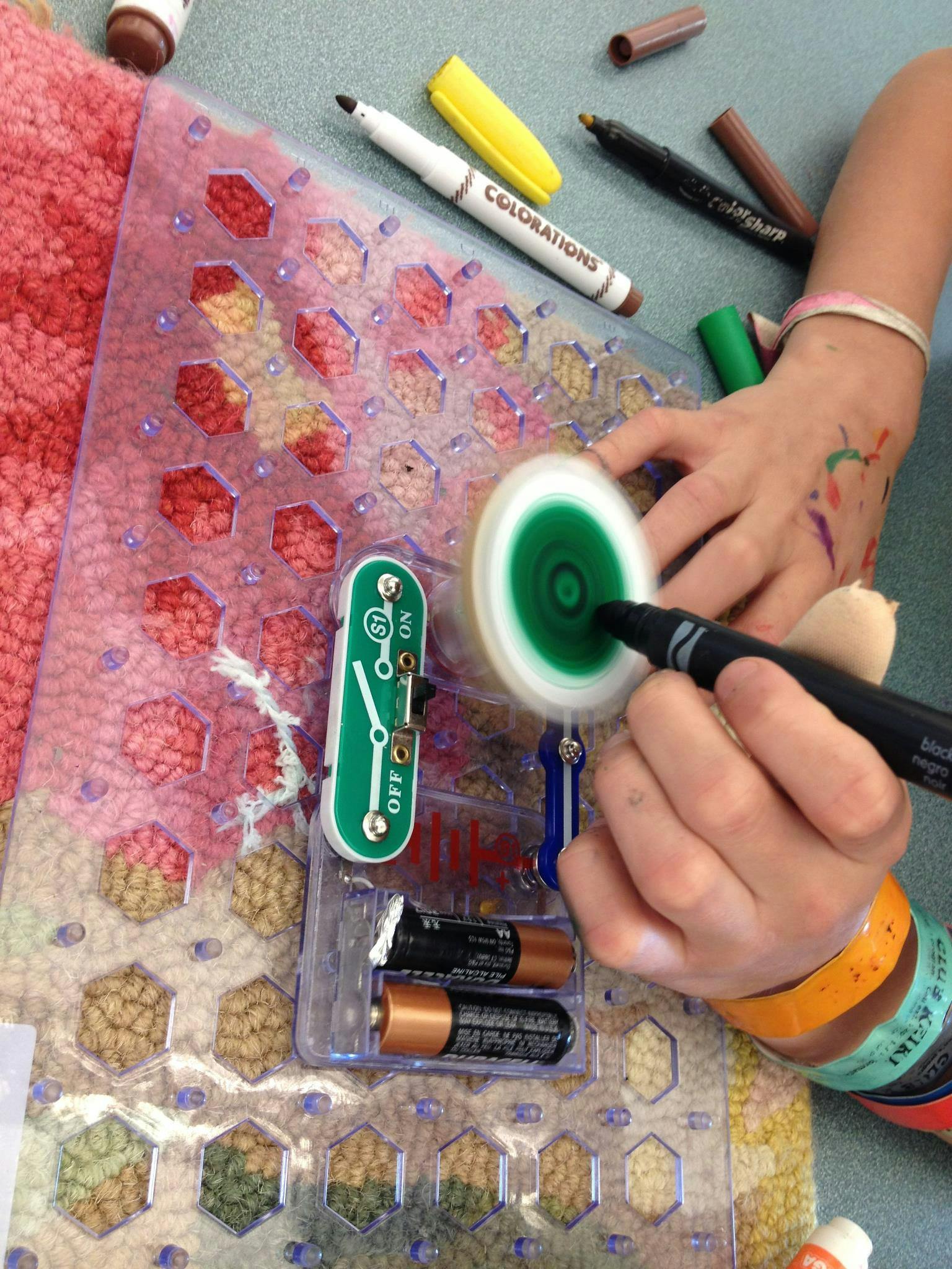 Person's hands coloring a spinning white and green disc on a circuit board
