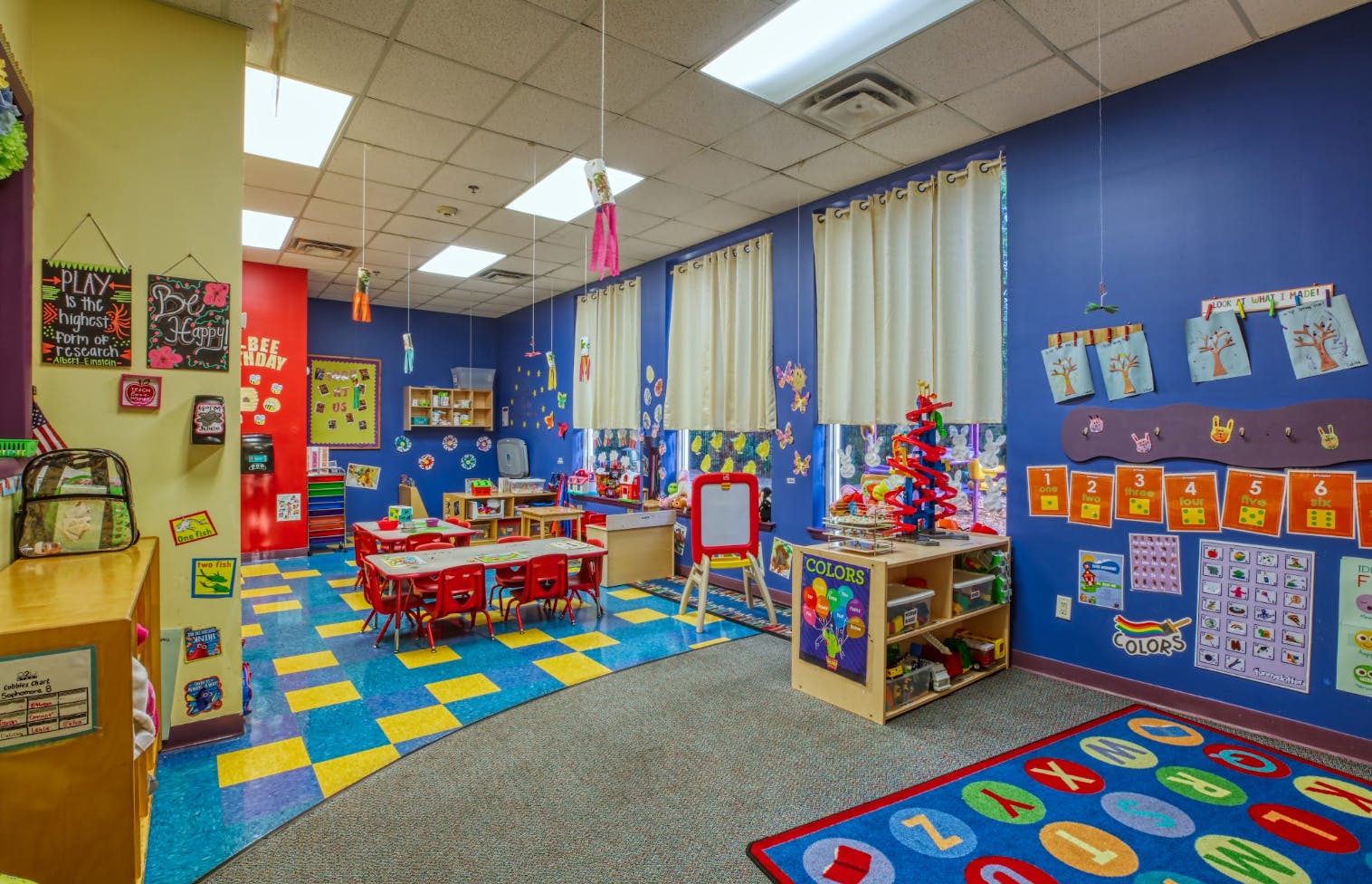 Colorful classroom with small red tables and chairs, toys, and educational posters