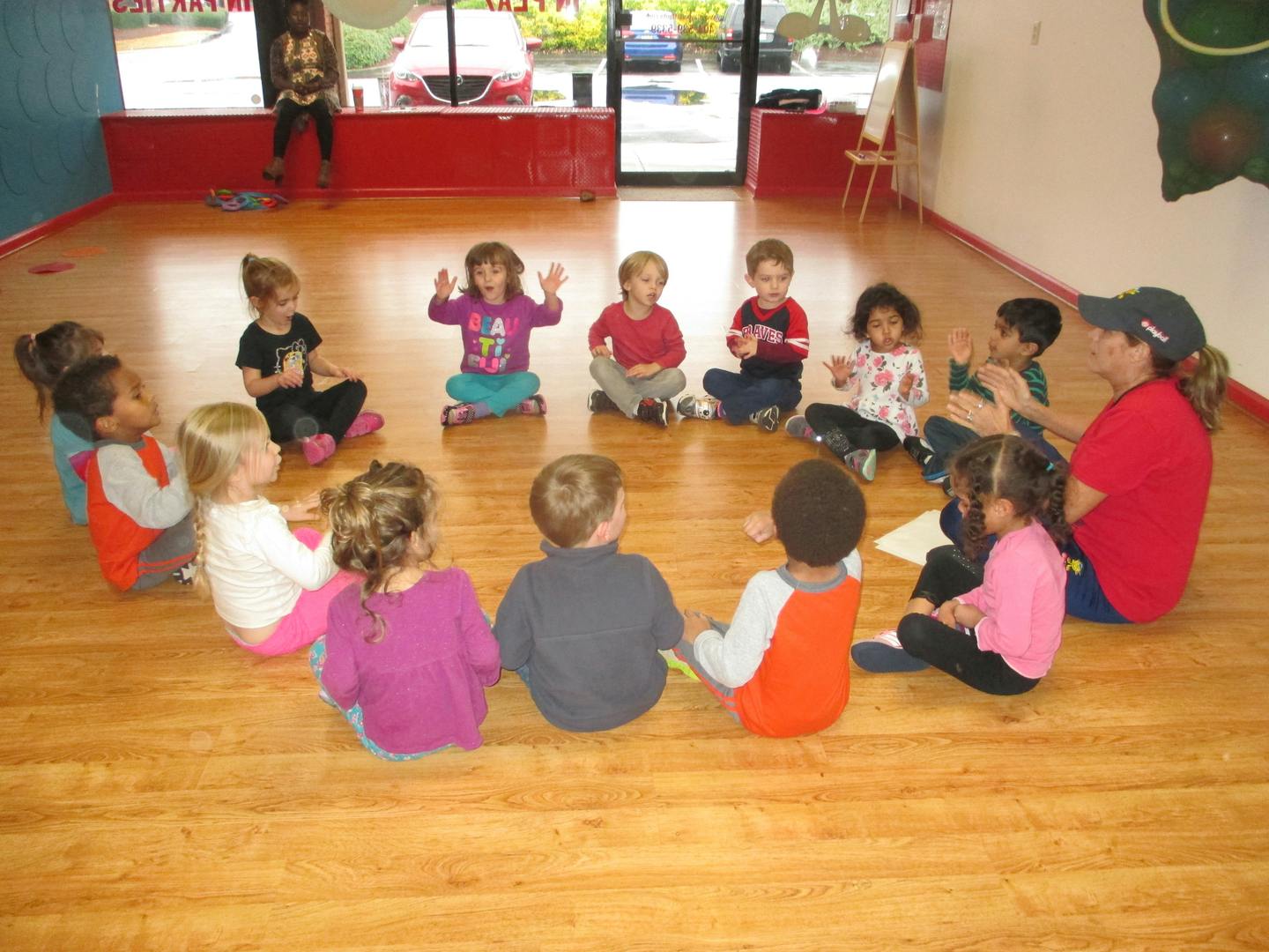 Children and an adult sitting in a circle on a wooden floor
