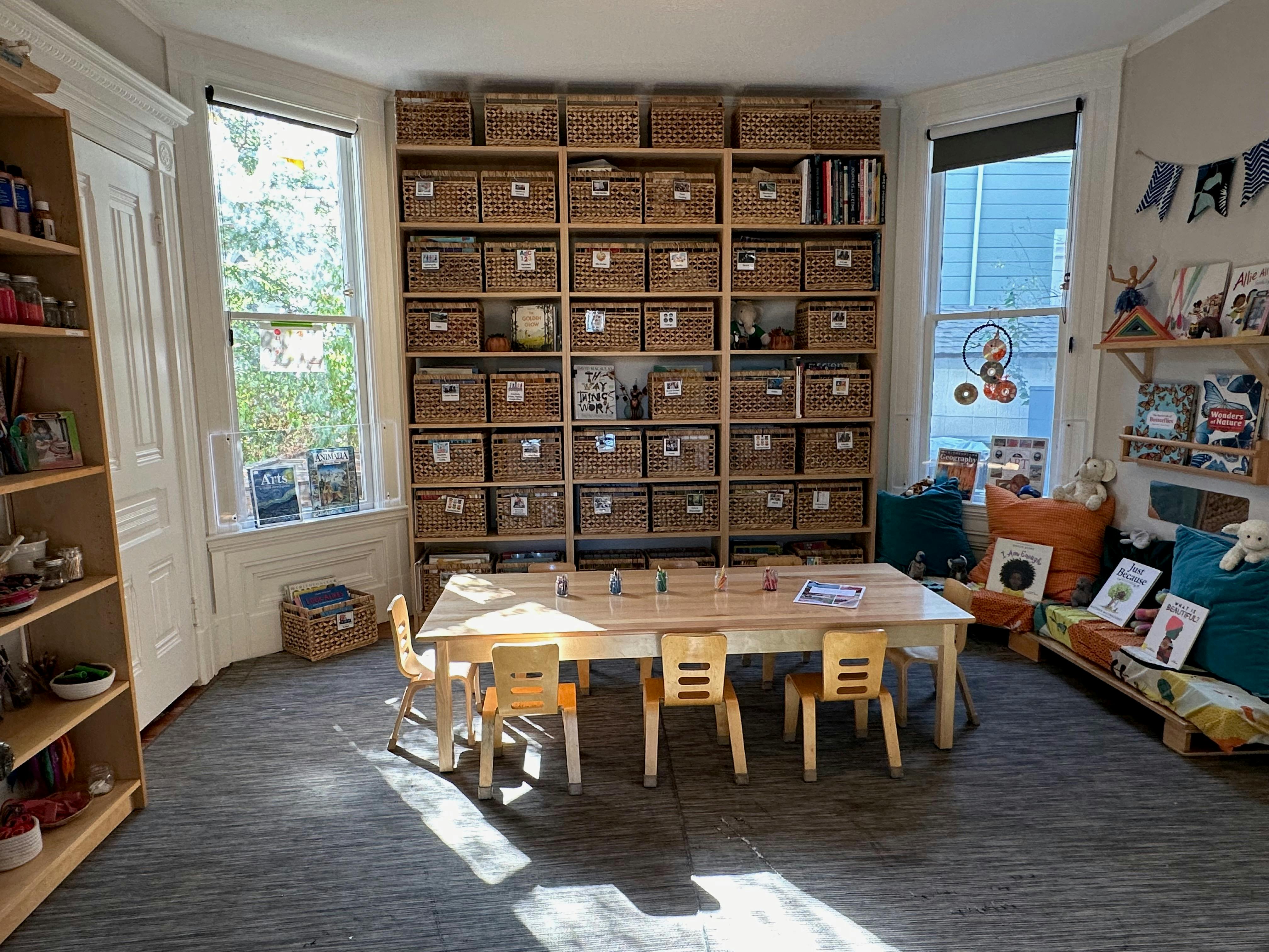 Classroom with a long wooden table and small chairs, shelves with baskets