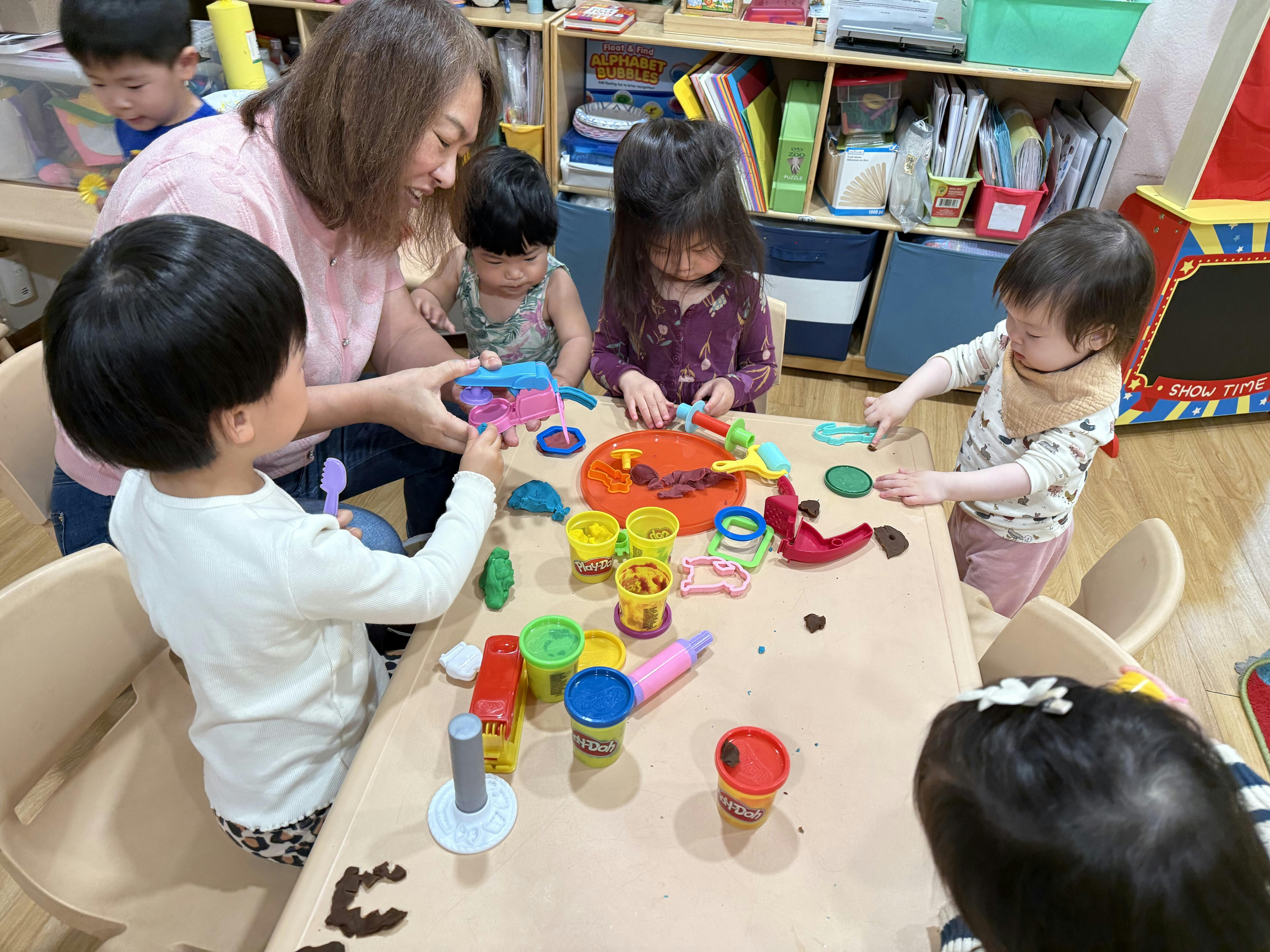 Adult and several children playing with Play-Doh at a table in a classroom
